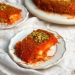 slice of knafeh with crispy pastry and melted cheese inside on a small plate, another plate in the background