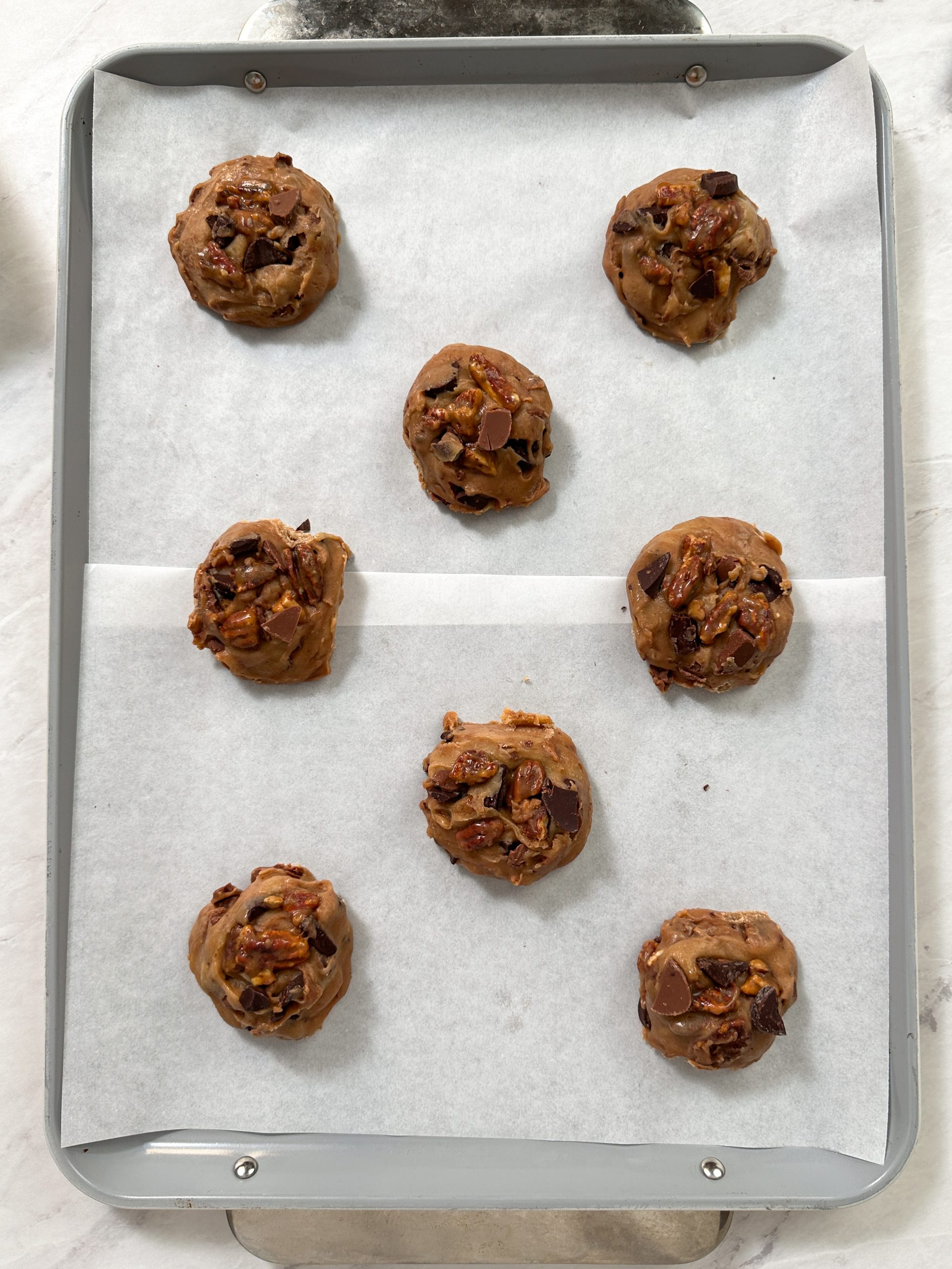 8 salted caramel pecan chocolate chip cookie dough balls placed on a cookie sheet with parchment paper