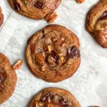 salted caramel pecan chocolate chip cookies placed side by side with some pecans scattered. cookies are a deep golden color and look crispy and chewy with puddles of chocolate; focus on one cookie with 4 in corners