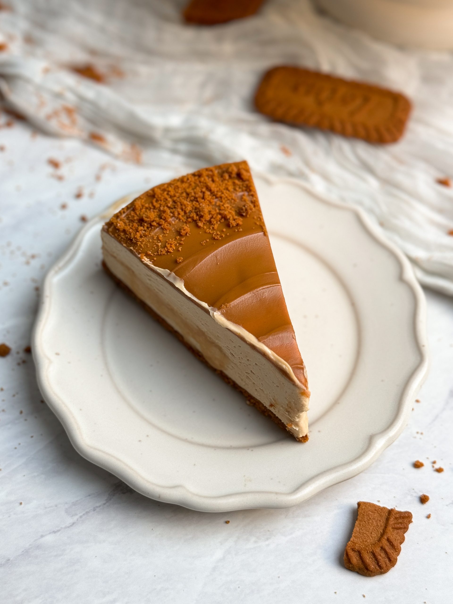 A slice of biscoff salted caramel cheesecake on a small plate with biscoff cookie butter on top