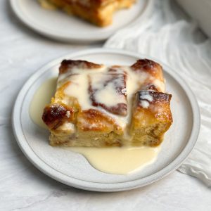 a slice of vanilla bread pudding on a small plate, with creme anglaise poured on top, Another plate seen in background