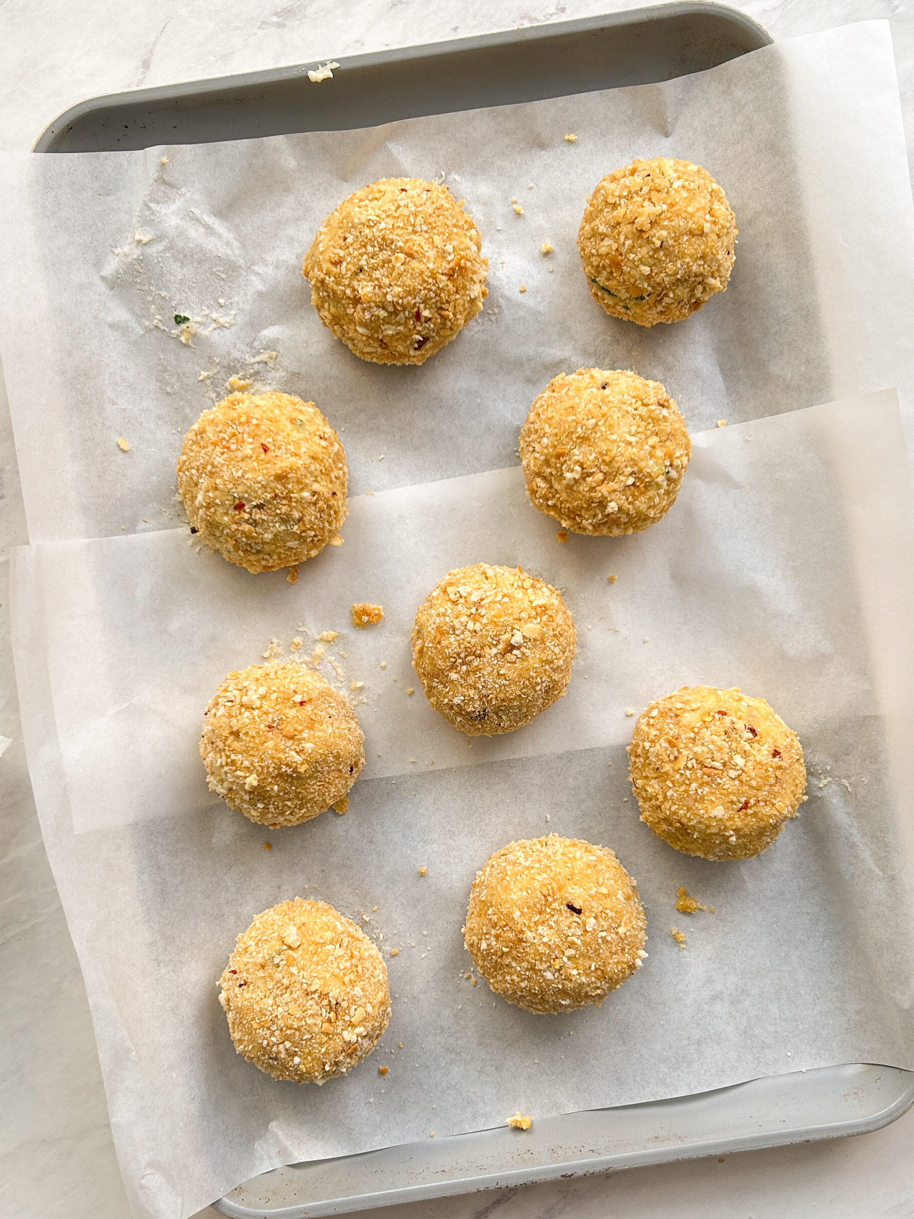 9 mashed potato balls coated with crushed crackers on a baking sheet