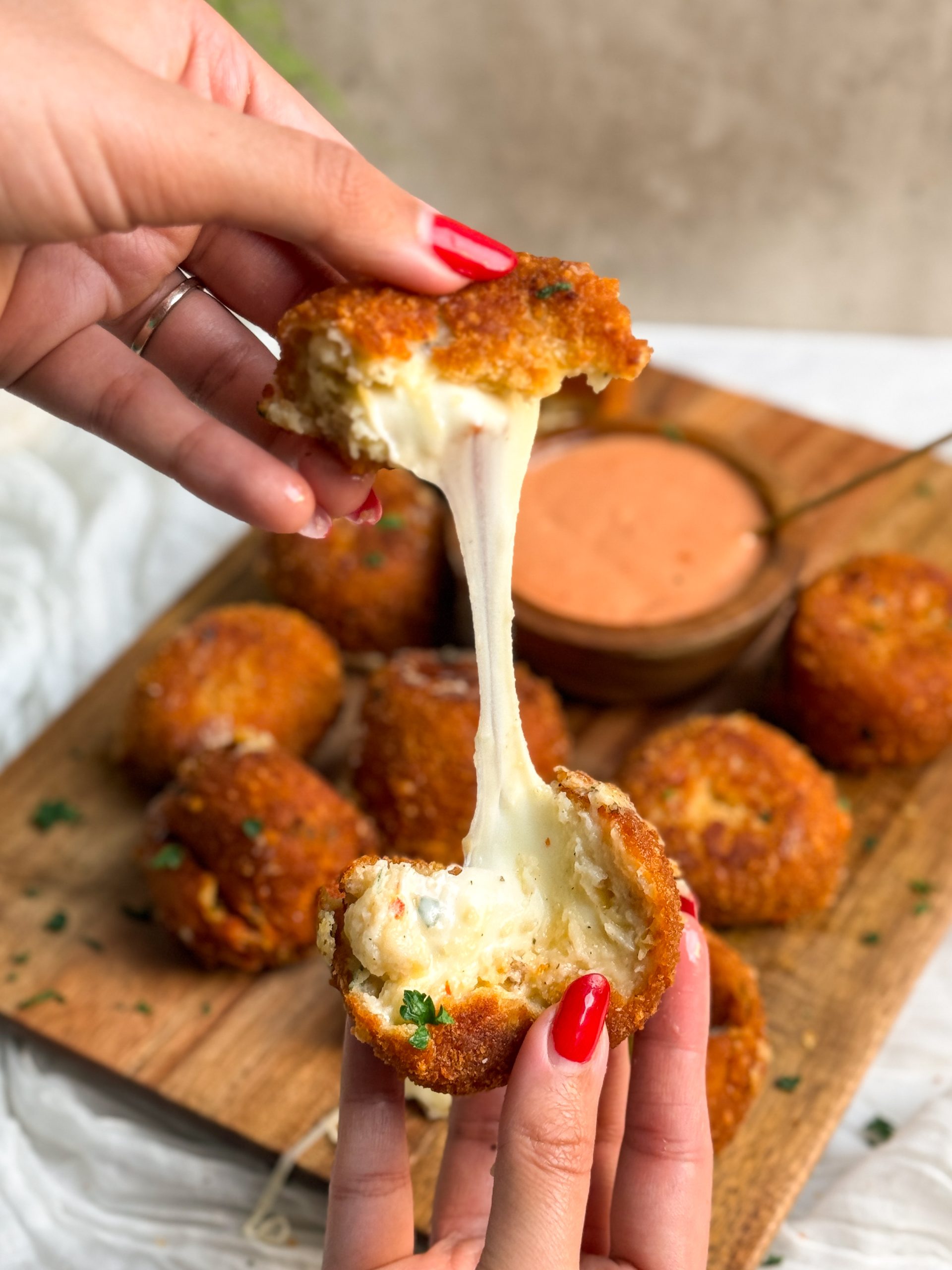 hands pulling a mashed potato ball in half with a cheese string in the middle