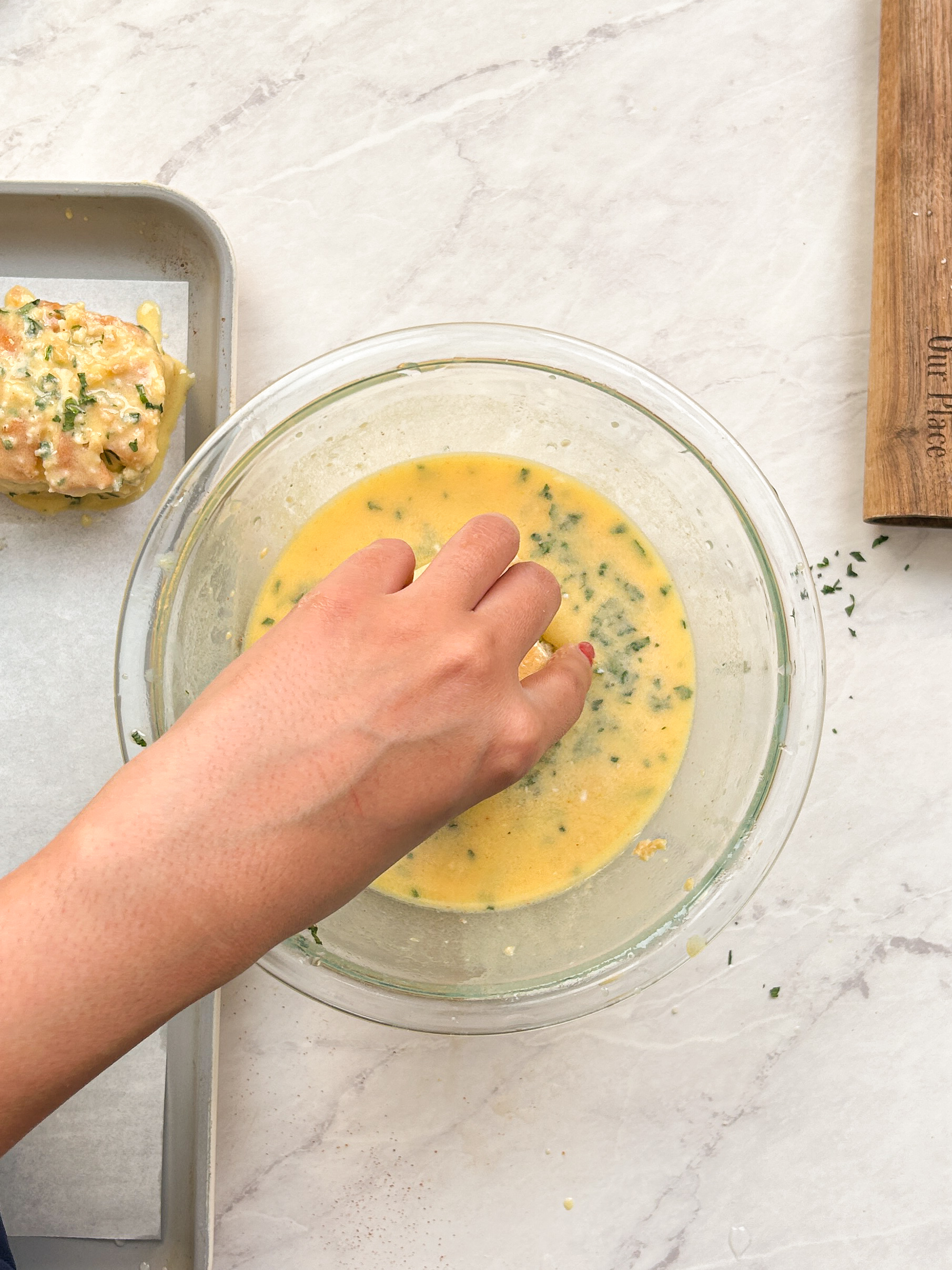 hand dipping a roll inside the garlic butter custard in a glass bowl