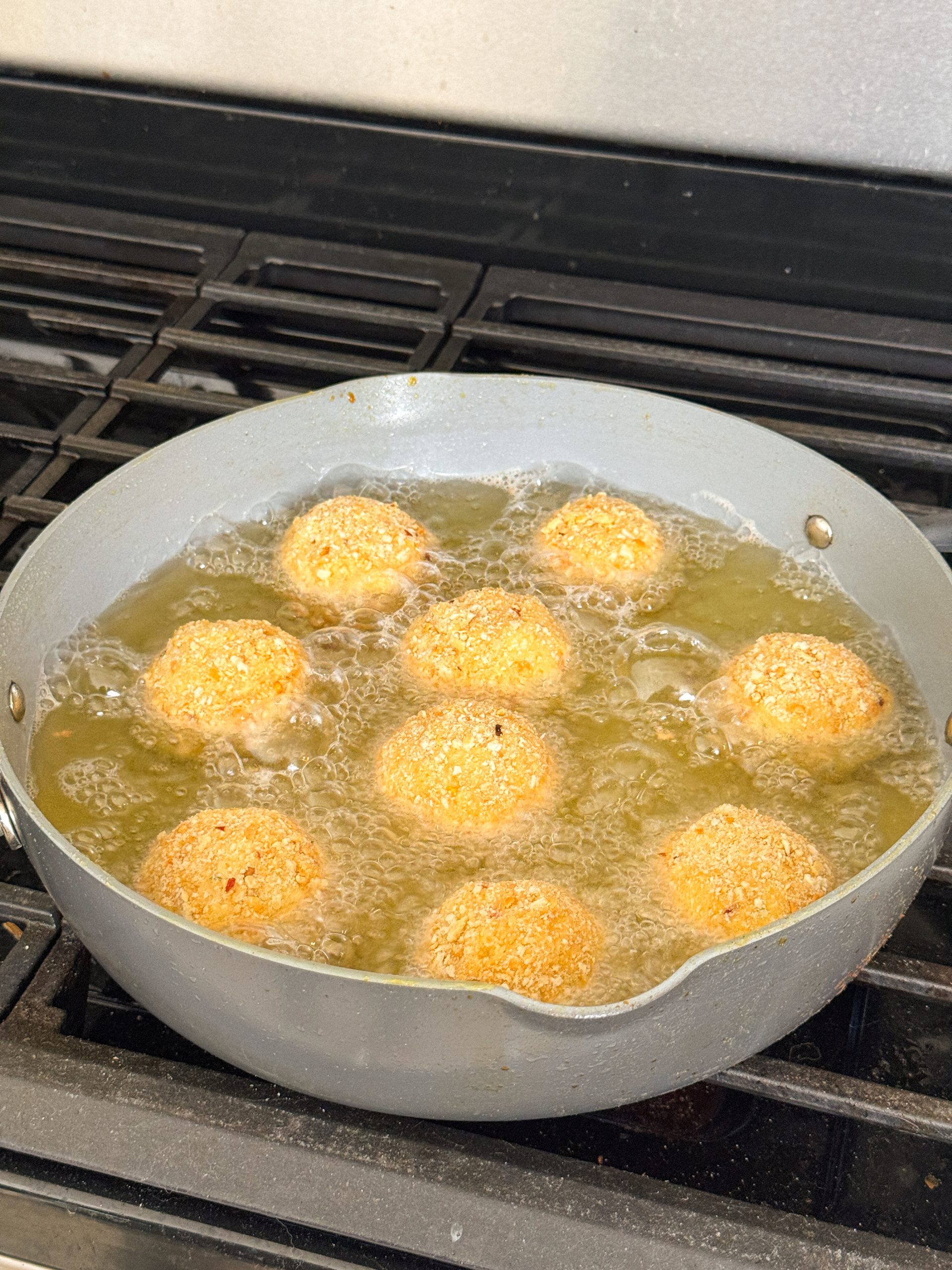 mashed potato balls being fried in a large skillet