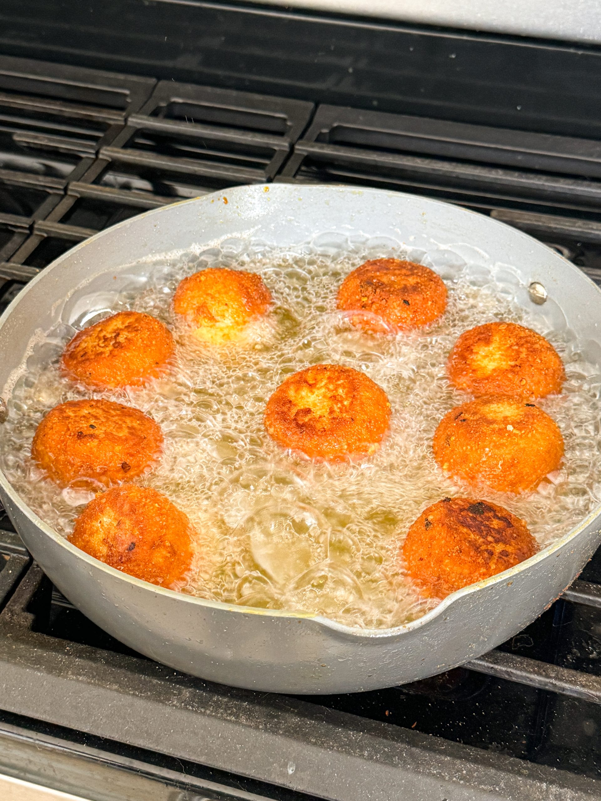 mashed potato balls being fried in a large skillet; balls have a golden color on them