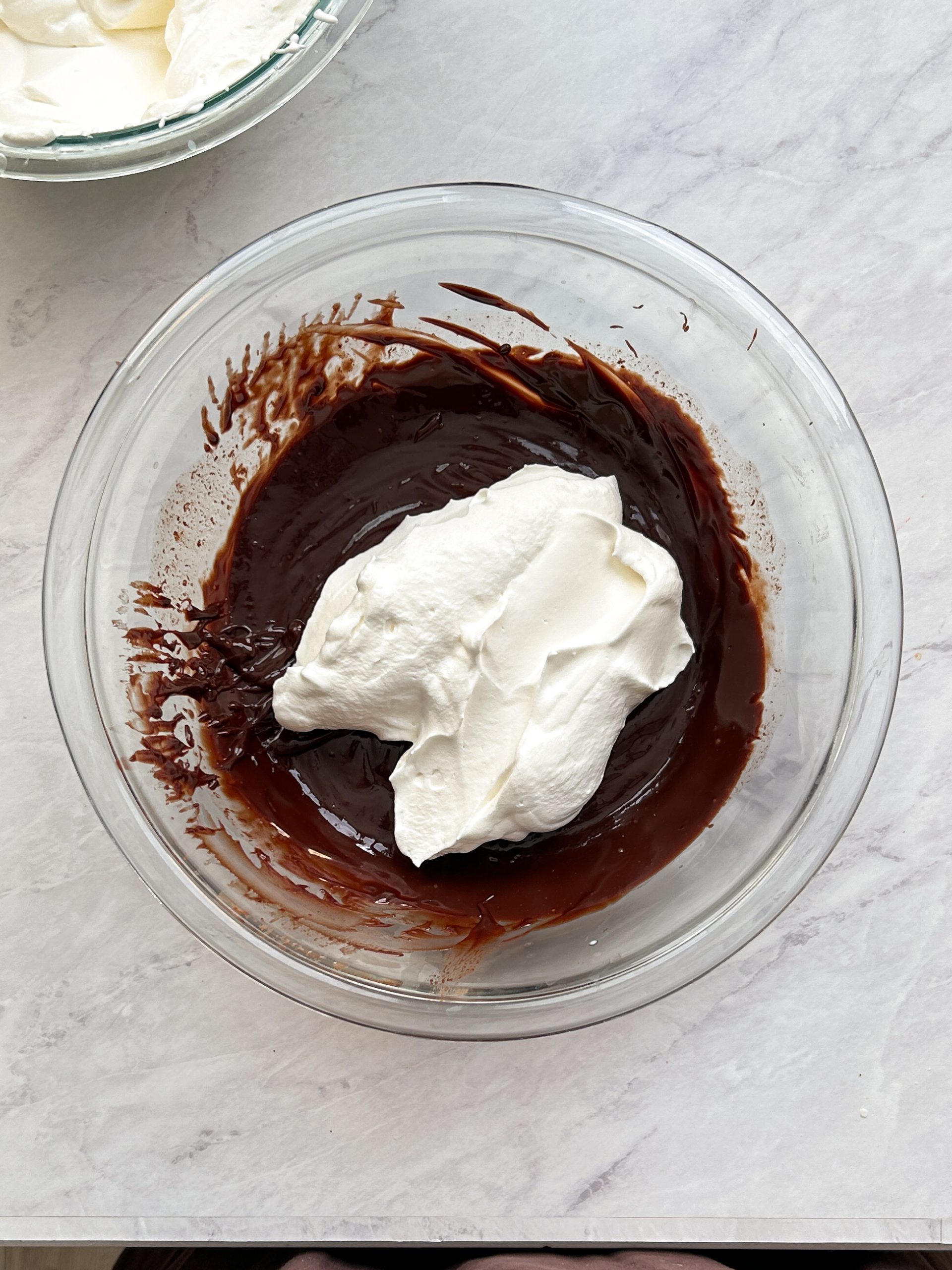 whipped cream added to chocolate ganache in a glass bowl