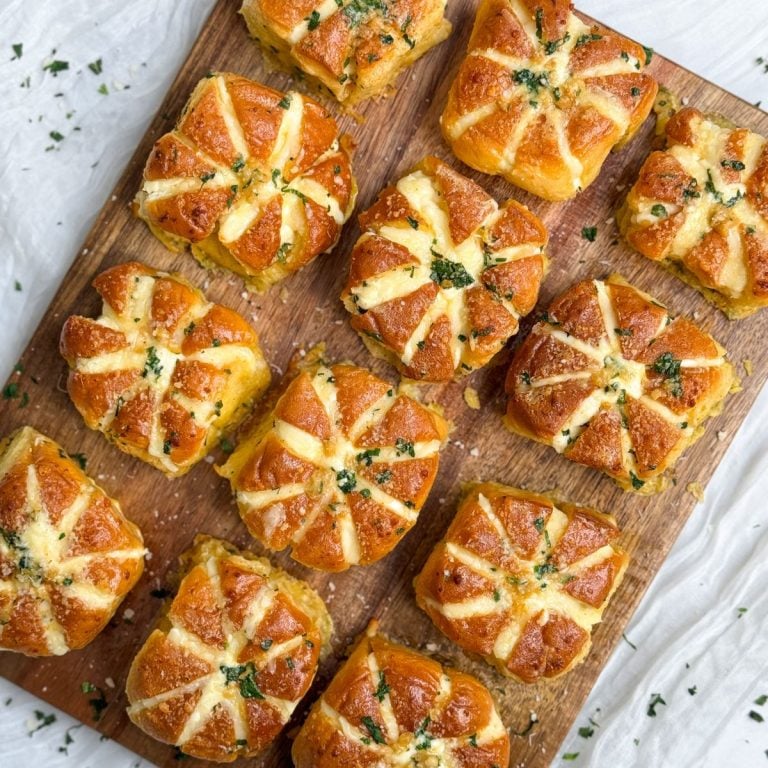 12 korean cream cheese garlic buns on a wooden cutting board. they are filled with cream cheese and topped with garlic and parmesan with a beautiful golden color