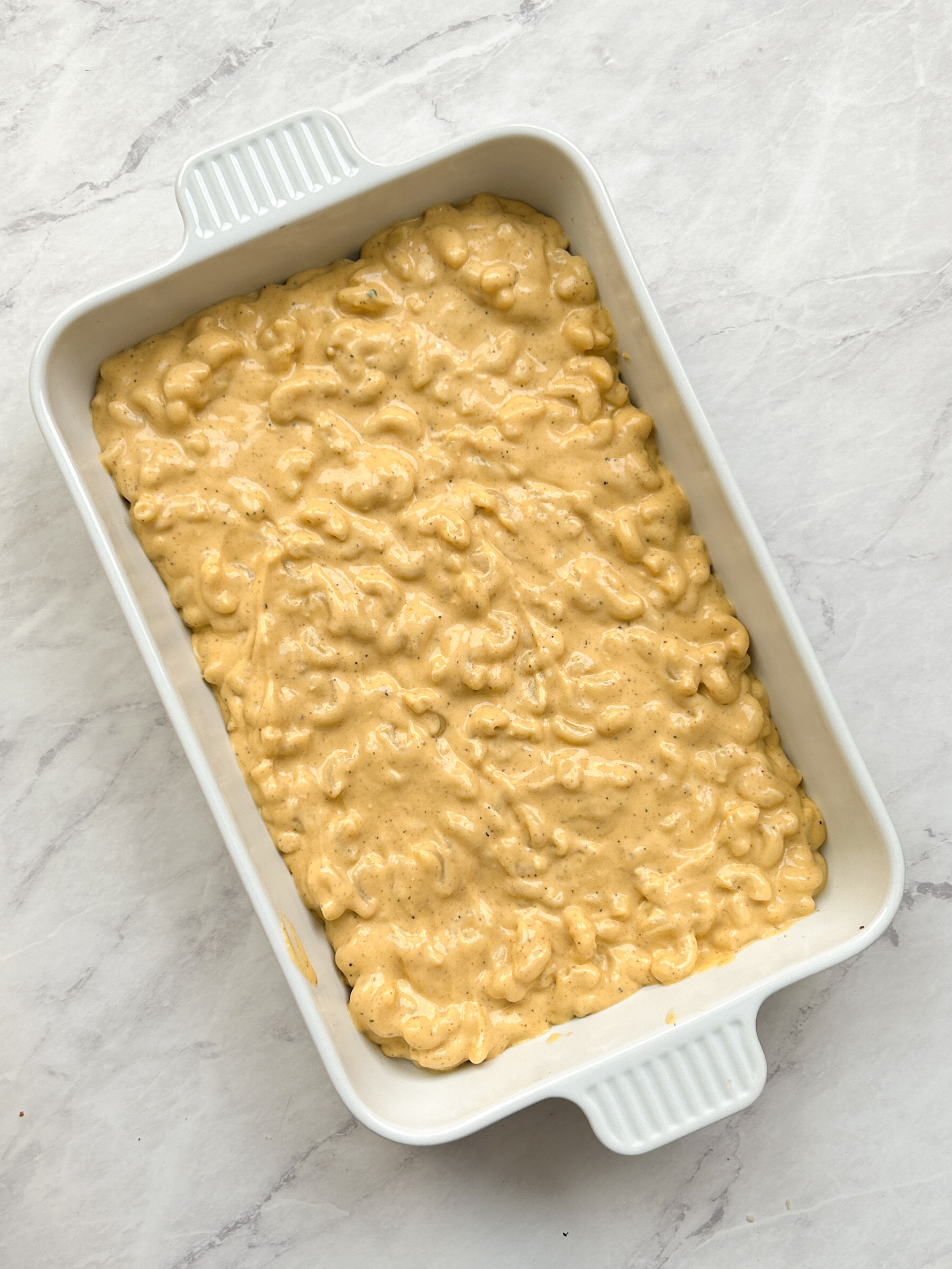 a layer of mac and cheese added to a white casserole dish
