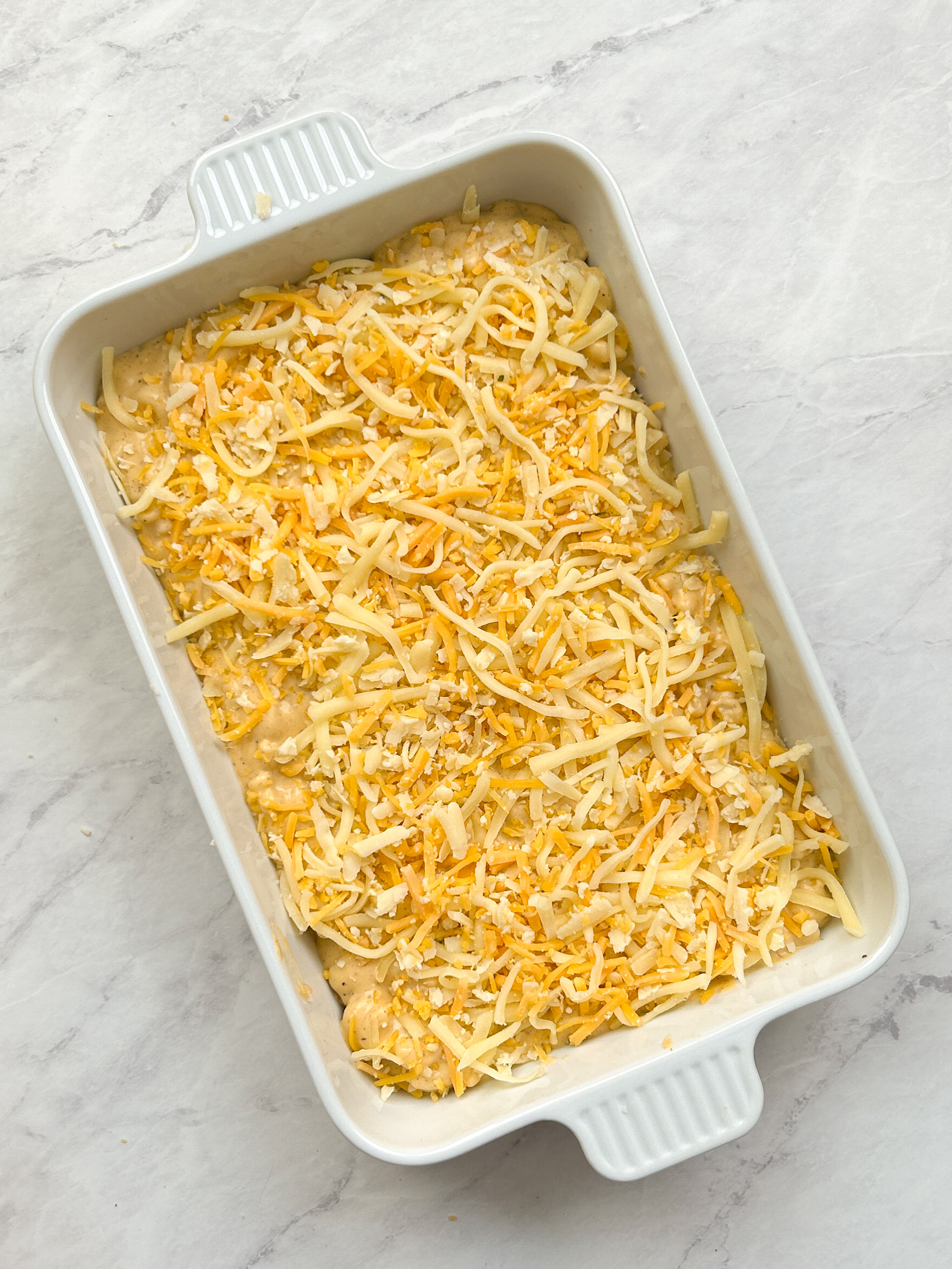 a layer of mac and cheese topped with a layer of shredded cheese in a white casserole dish