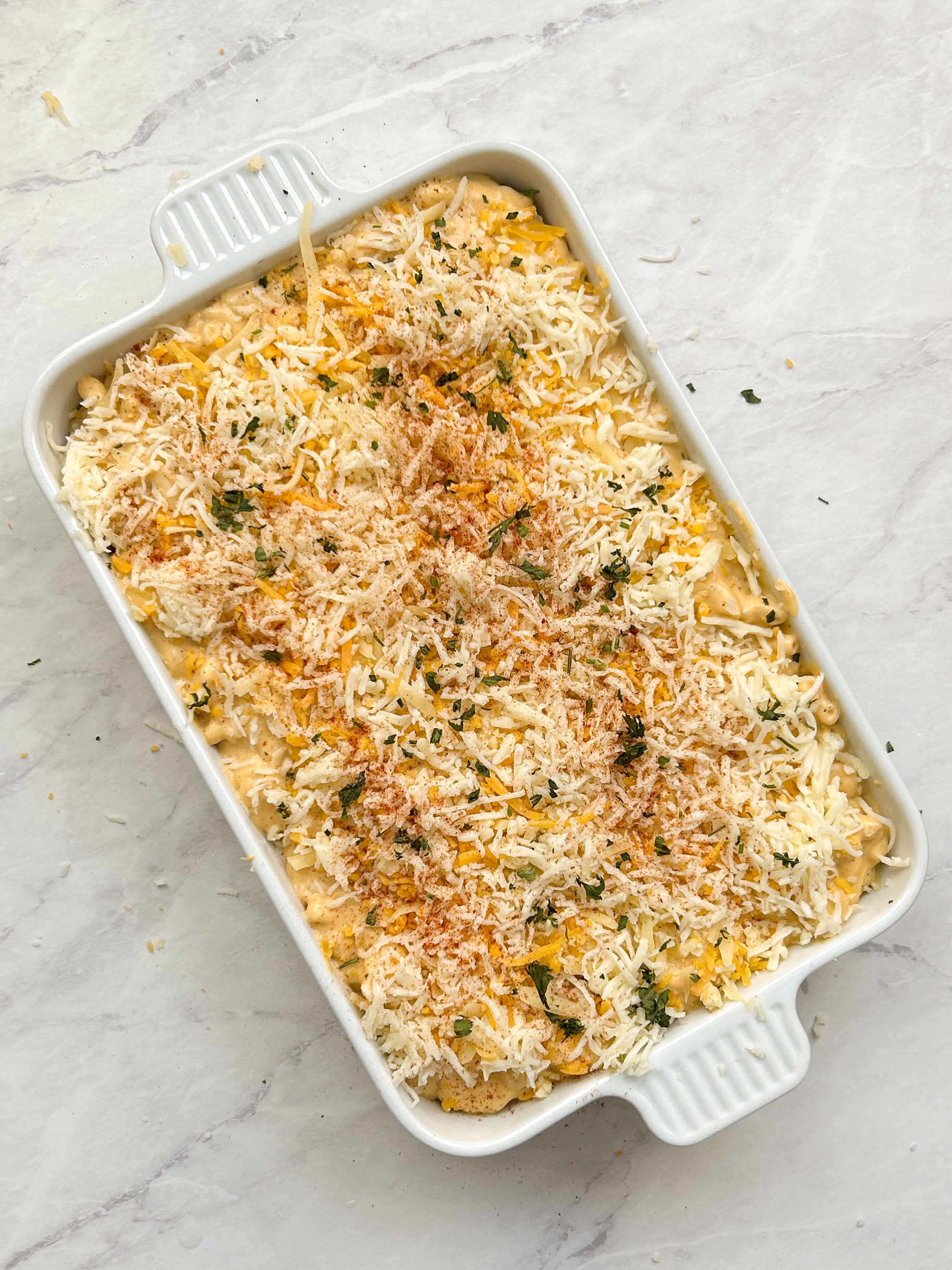 mac and cheese layered in a white casserole dish topped with shredded cheese, parsley and paprika