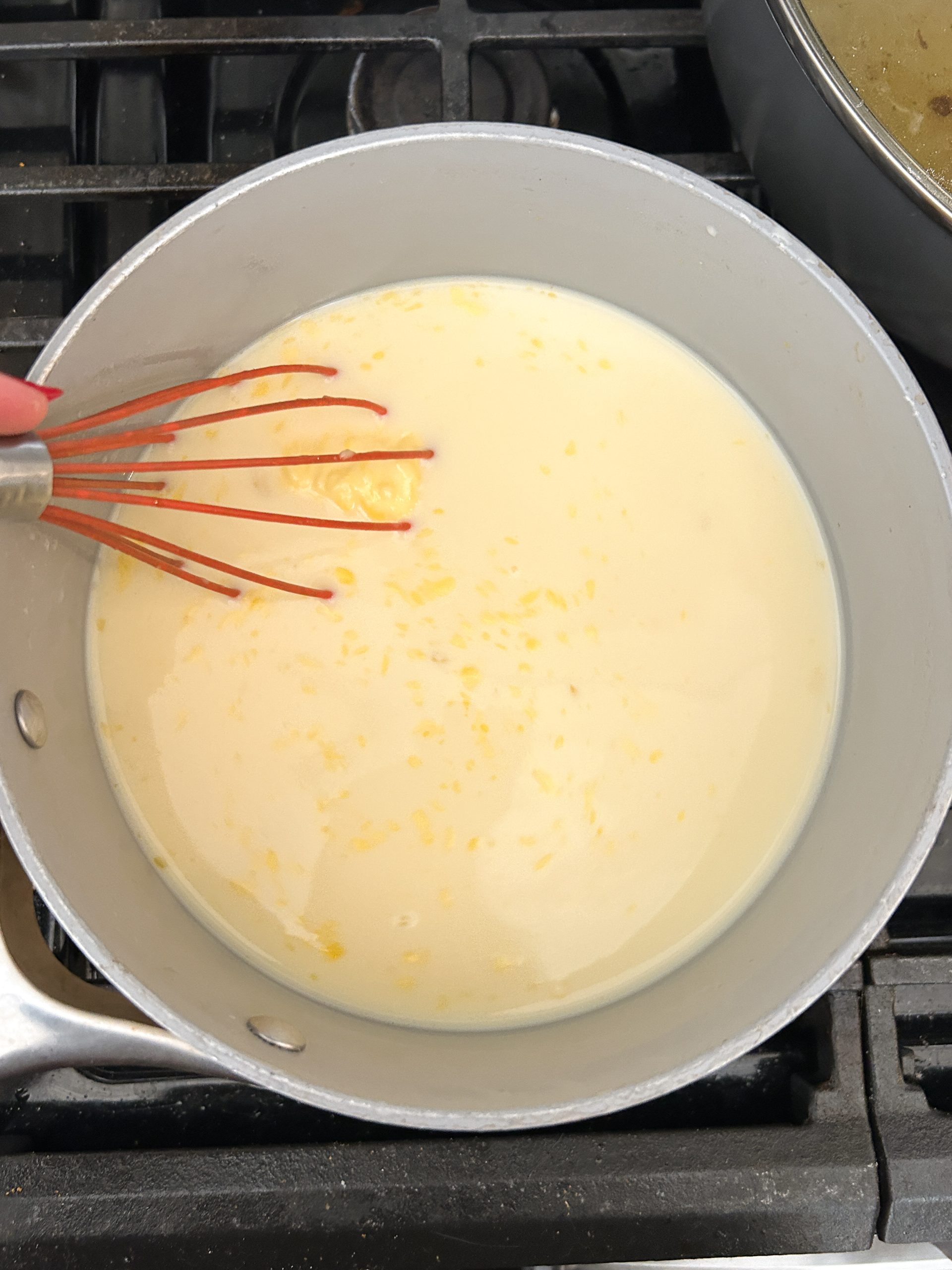 vanilla custard sauce ingredients in a saucepan with a whisk inside, ingredients have just combined