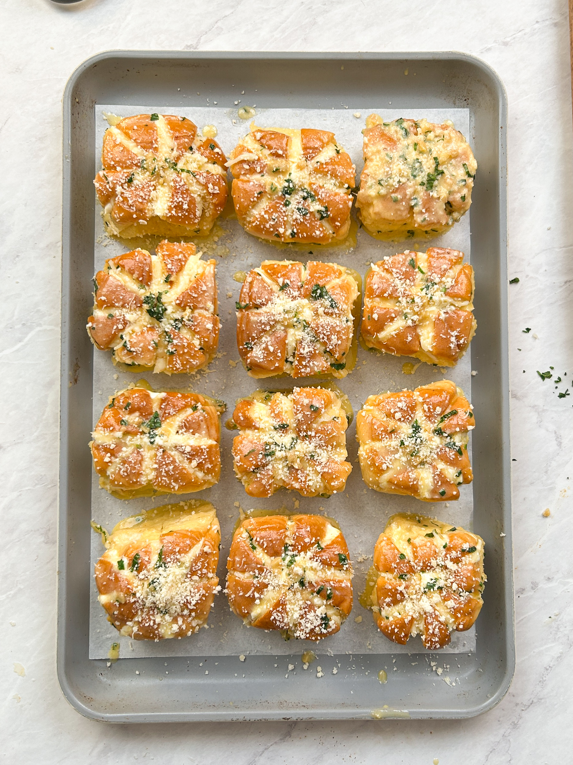 12 korean cream cheese garlic buns filled with cream cheese, dipped in garlic custard, and topped with parmesan cheese on a baking sheet
