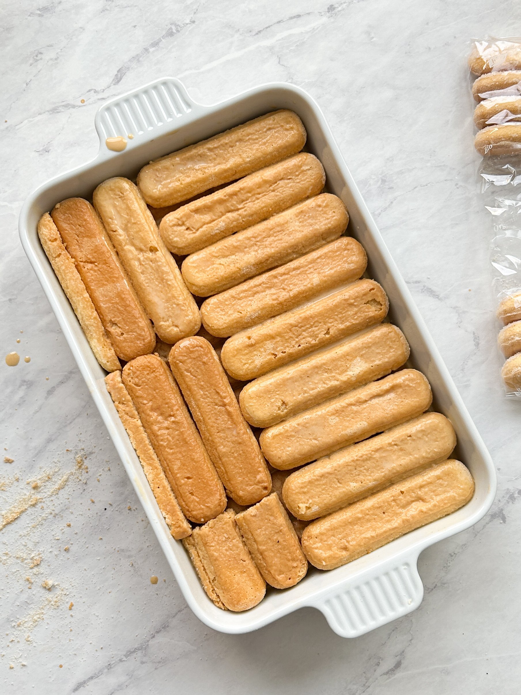 baking ceramic dish with 2 layers of ladyfingers drenched in chai tres leches milk mixture