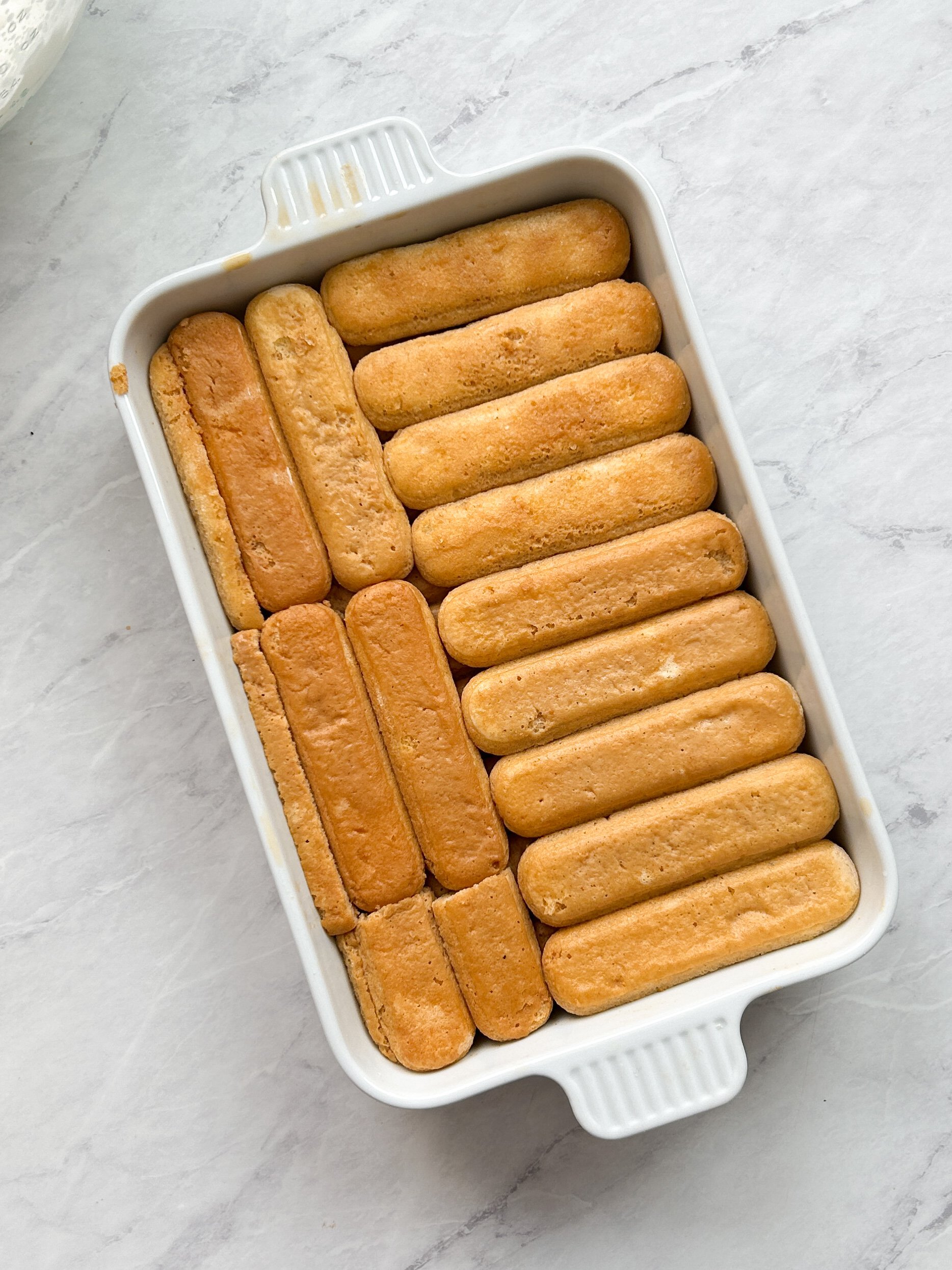 baking ceramic dish with 2 layers of ladyfingers soaked in chai tres leches milk mixture