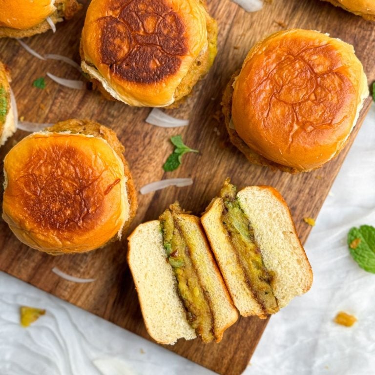 bun kababs on a cutting board. one is cut into half and placed sideways to show the potato patty and chutneys inside