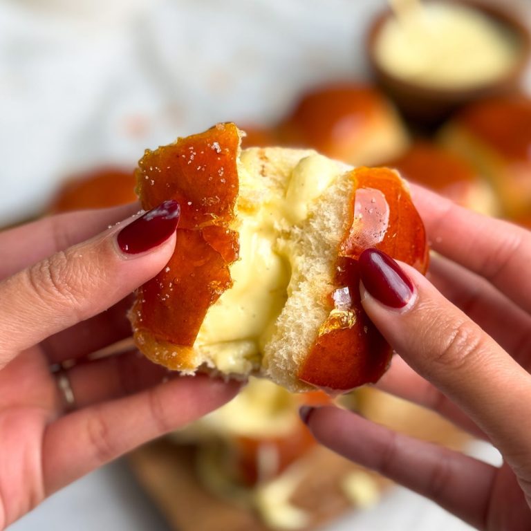 two hands holding a creme brulee donut roll, breaking it half so the caramal coating cracks and revealing the custard filling inside. more donut rolls seen in the background