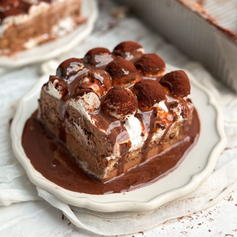 a square slice of hot chocolate tiramisu with hot chocolate poured top on a small plate, picture from the side showing layers of ladyfingers and hot chocolate mascarpone cream. hot chocolate is pouring off the side