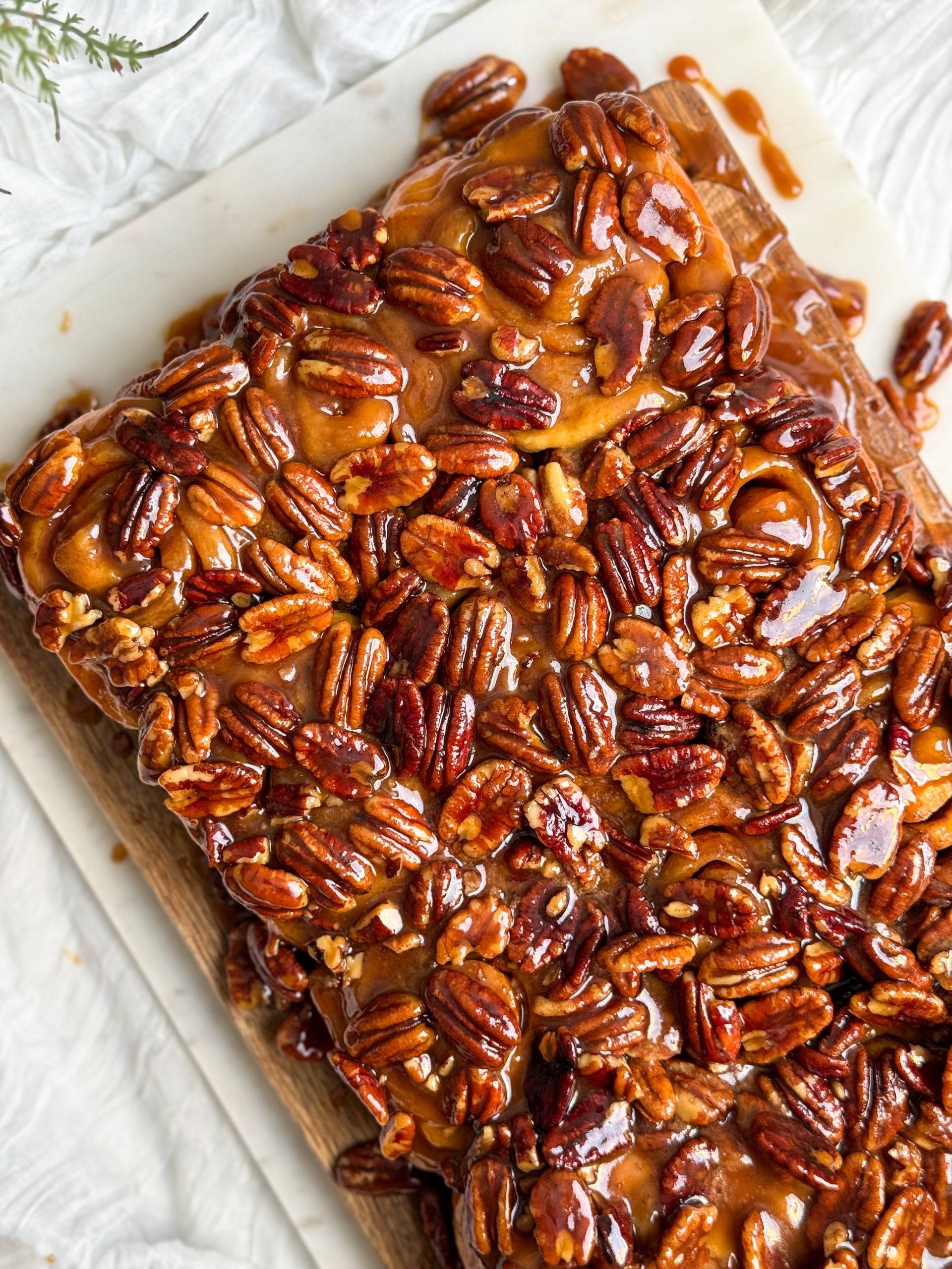 12 sticky pecan cinnamon buns with a caramel pecan topping on a wooden cutting board. they look soft and fluffy with a beautiful golden nutty topping. close up picture on the top