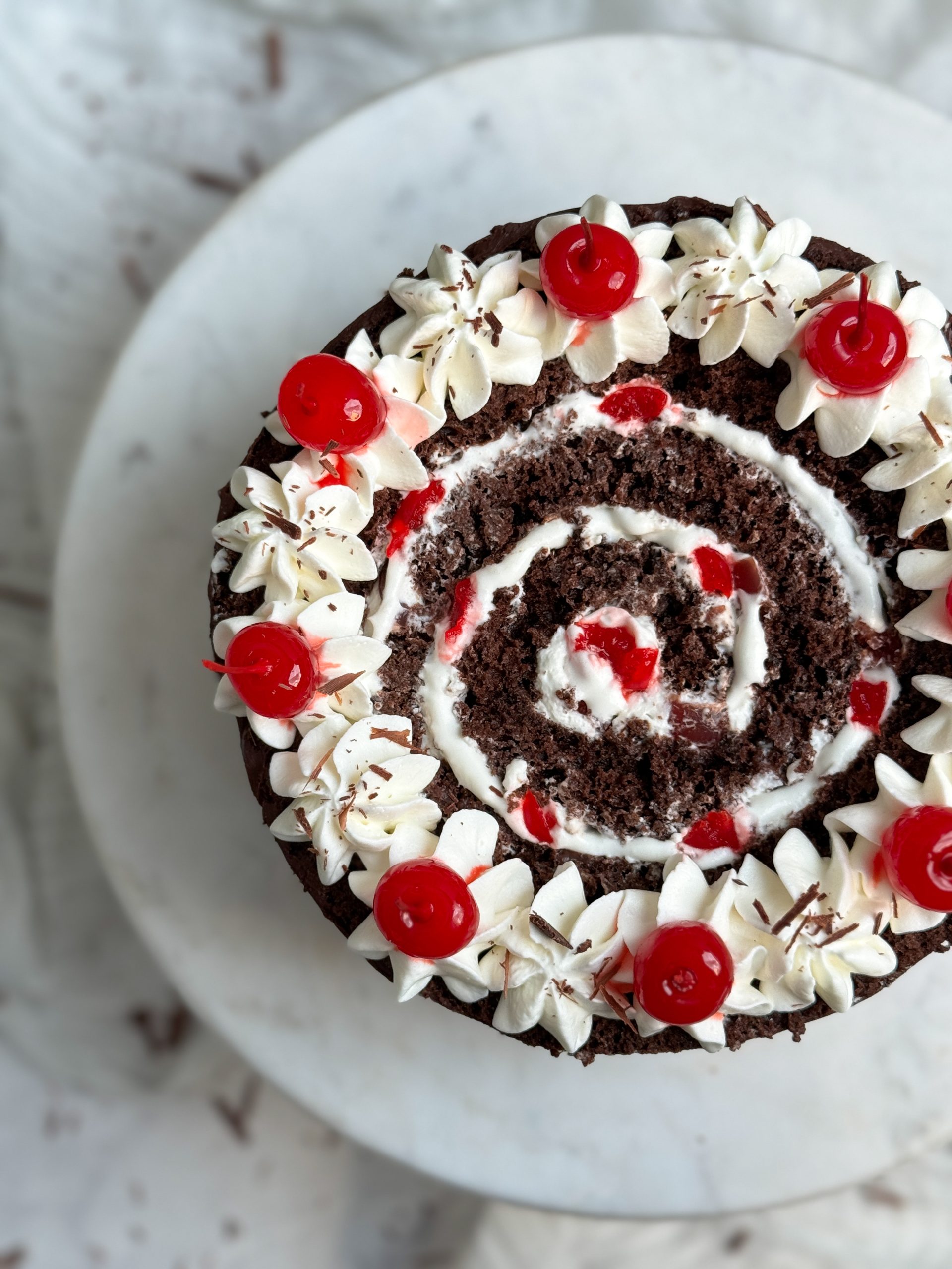 vertical black forest swiss roll cake from the top. the cake has a swirl of chocolate cake and whipped cream, with cream and cherries used for decoration on top. close up picture