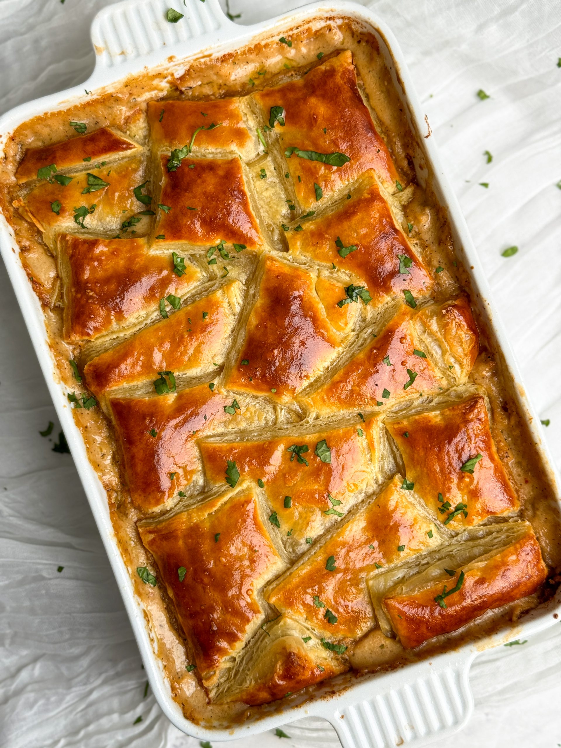 a rectangular dish with chicken pot pie inside. there are squares of golden crispy pastry arranged in a beautiful pattern on top of the pie, garnished with parsley