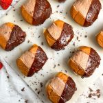 chocolate cream buns on a marble serving board. buns have a smooth filling of chocolate cream in the middle, and are dipped in shiny chocolate glaze on the side. picture shows the side of the board