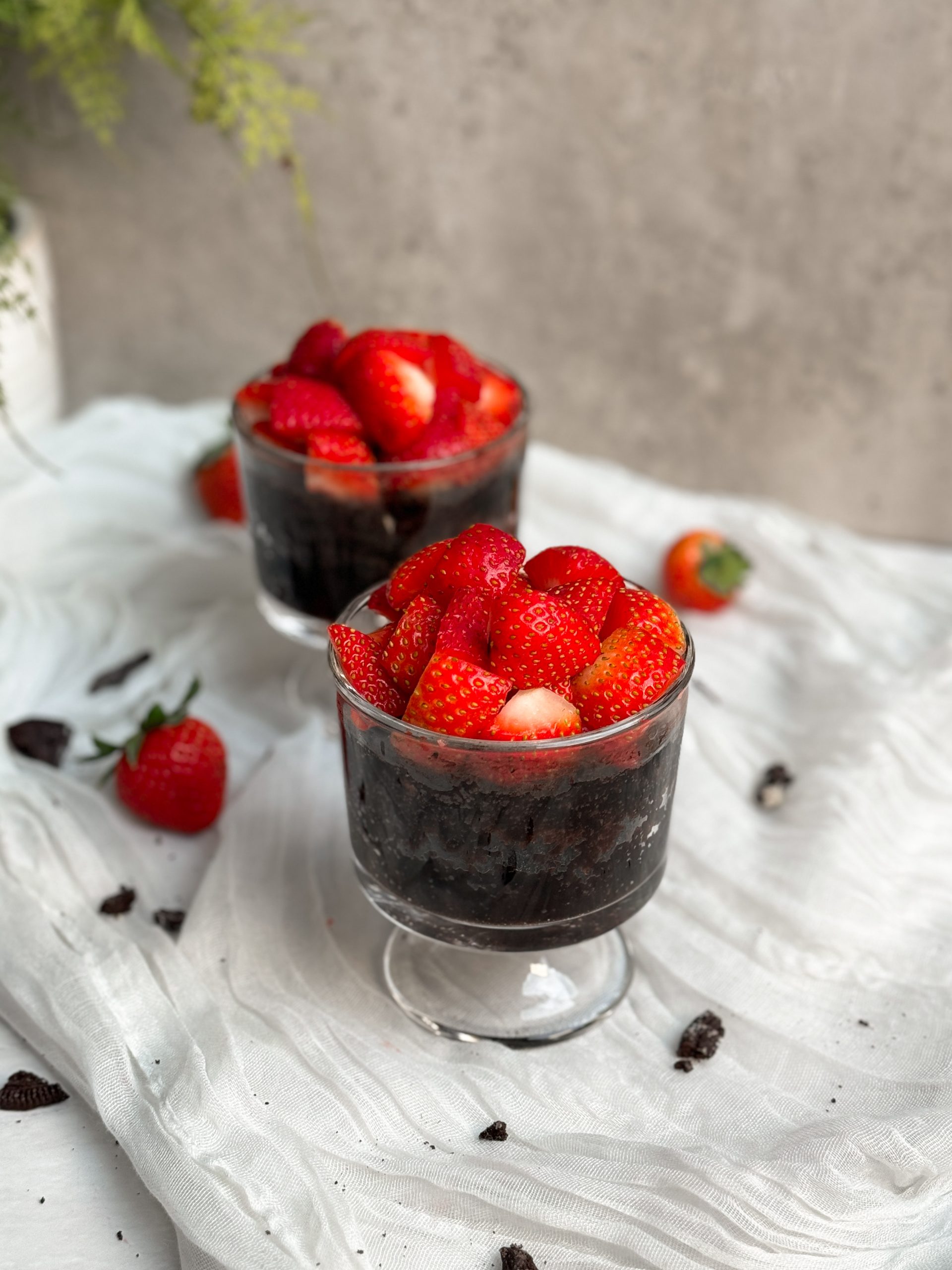 2 glass mugs with chocolate mug cakes inside, topped with chopped strawberries