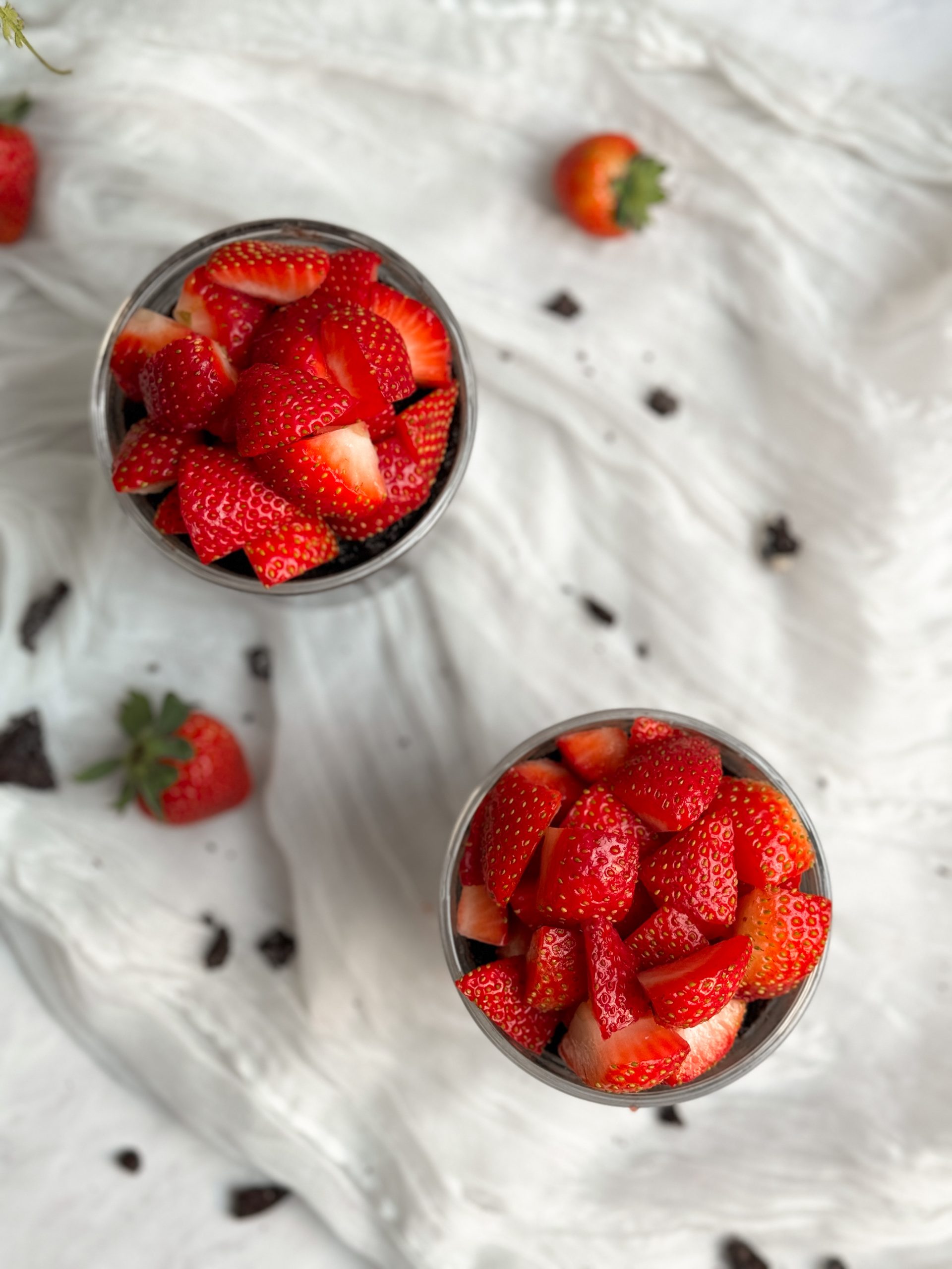 2 glass mugs with chocolate mug cakes inside, topped with chopped strawberries. picture from top
