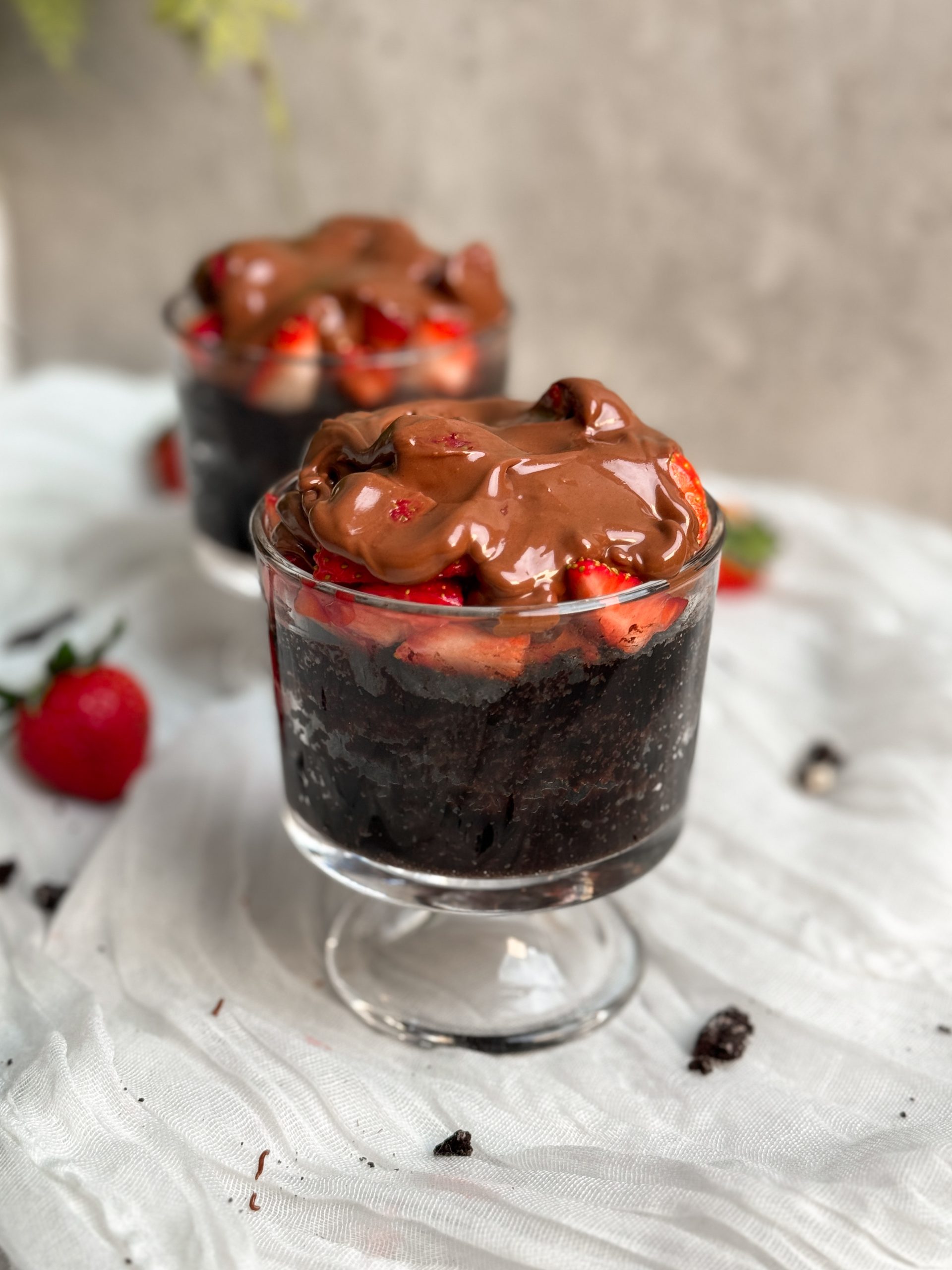 2 glass cups with chocolate strawberry mug cakes inside. moist chocolate cake topped with chopped strawberries and melted chocolate