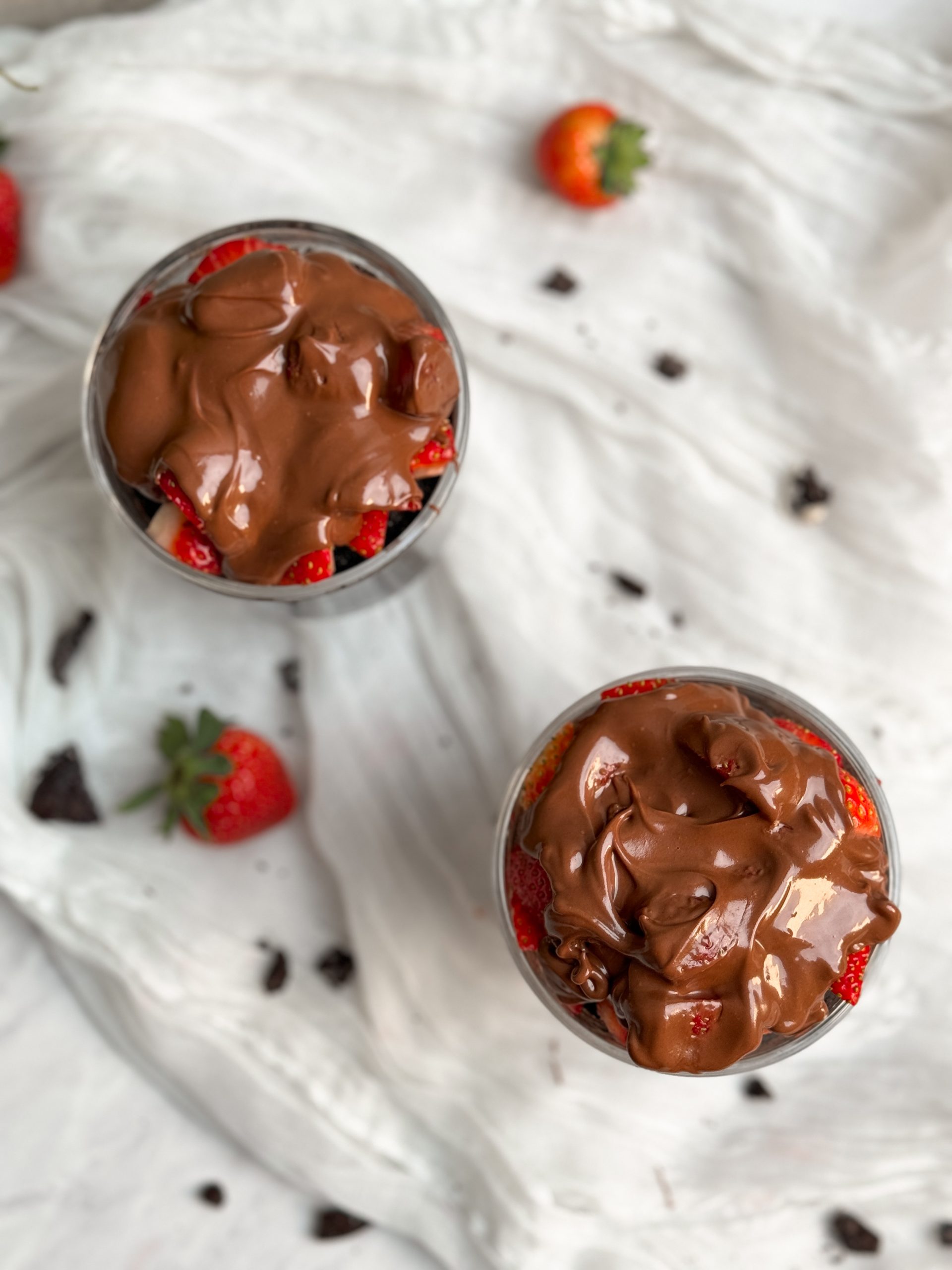 2 glass cups with chocolate strawberry mug cakes inside. moist chocolate cake topped with chopped strawberries and melted chocolate, picture from top