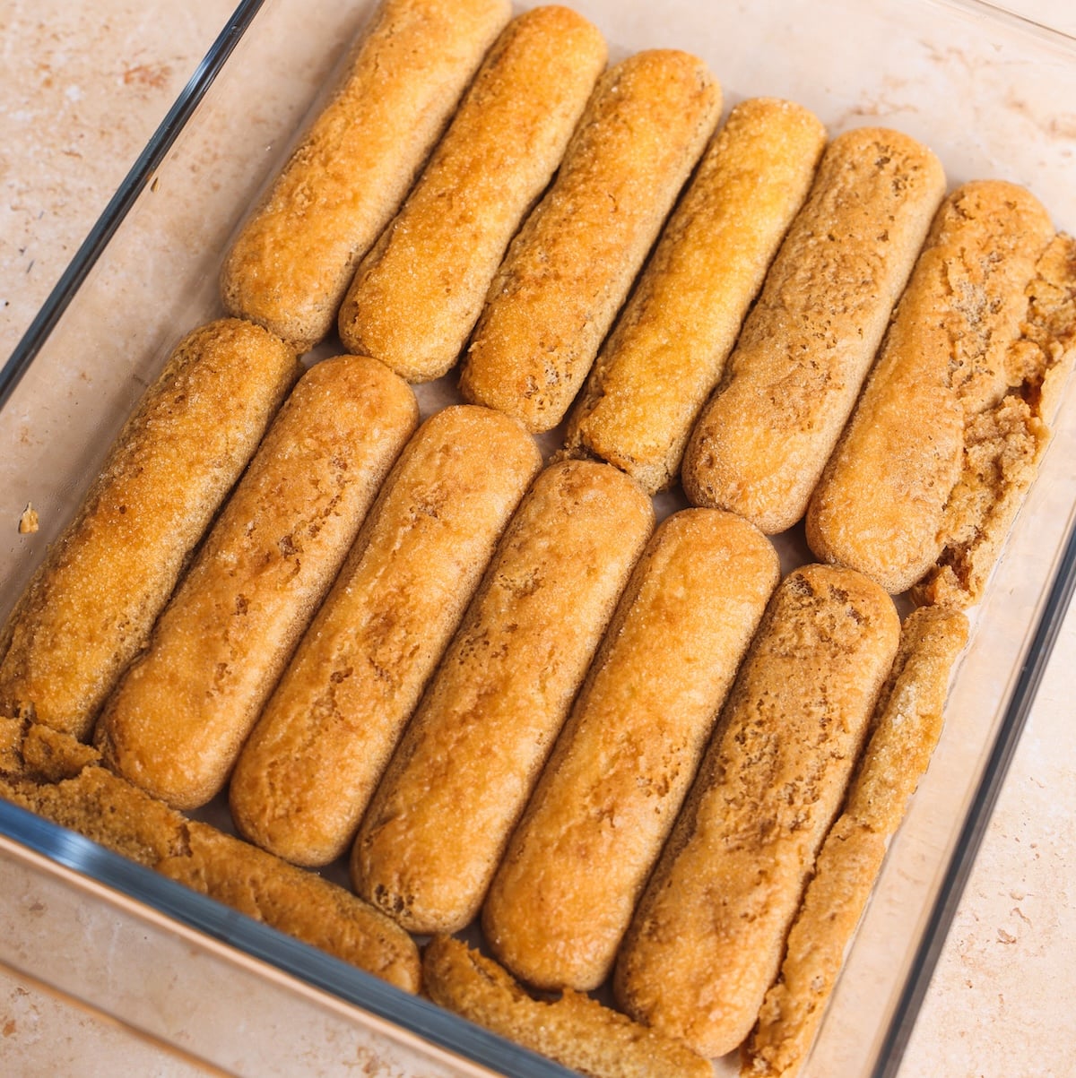A glass dish filled with ladyfinger cookies arranged in neat rows