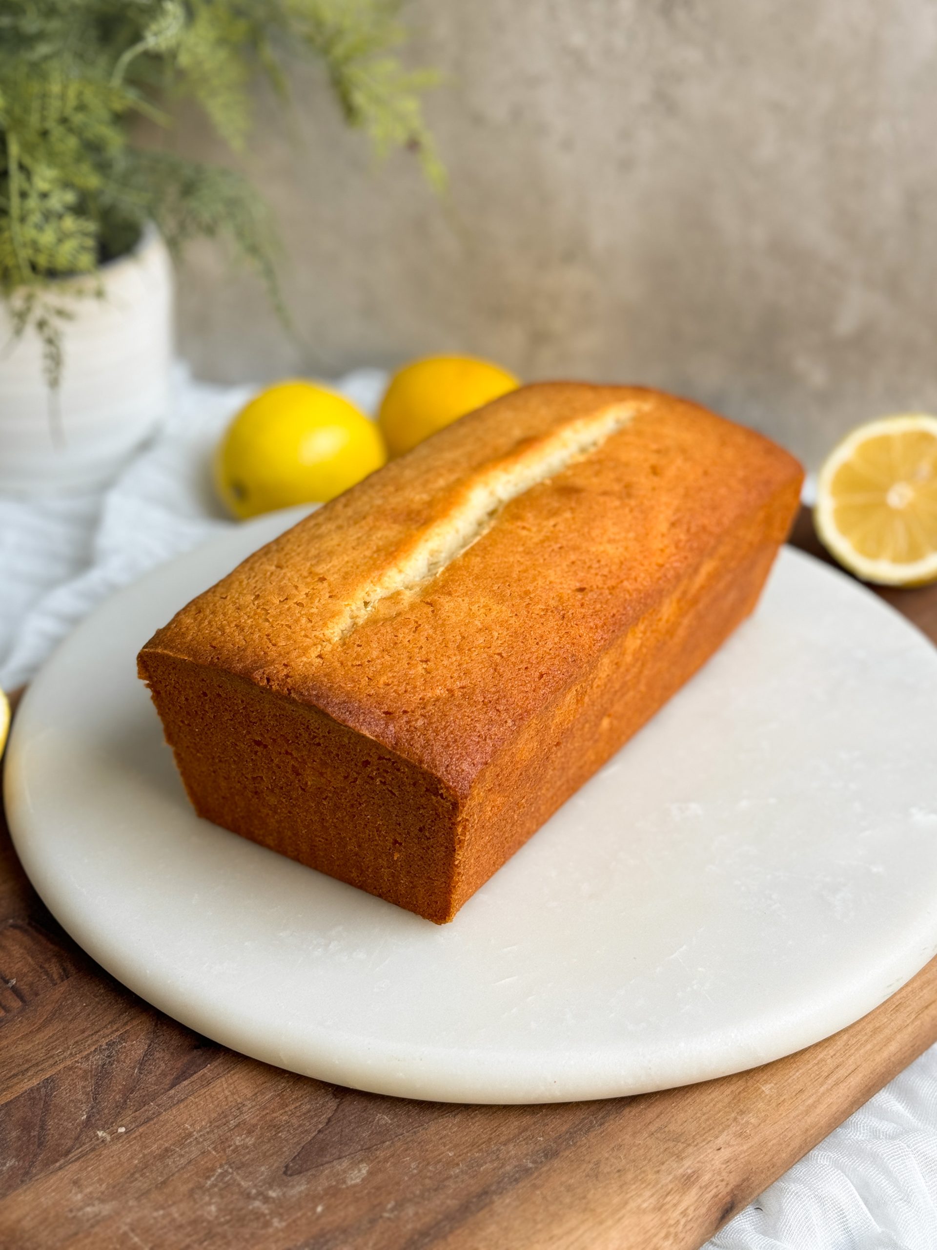 lemon loaf cake on a marble round serving board. cake has a beautiful golden color all over and a perfect crack down the middle