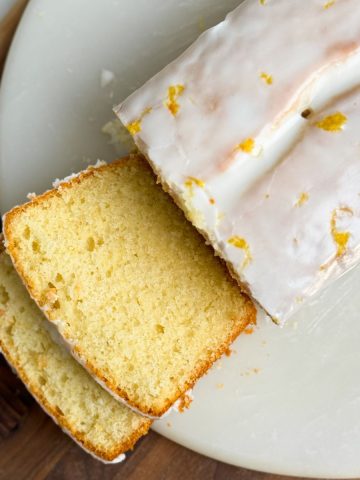 lemon loaf cake on a round marble serving board. cake has a beautiful color and is covered with lemon icing. 2 slices have been cut and are falling down showing the soft and moist interior. close up picture from the top
