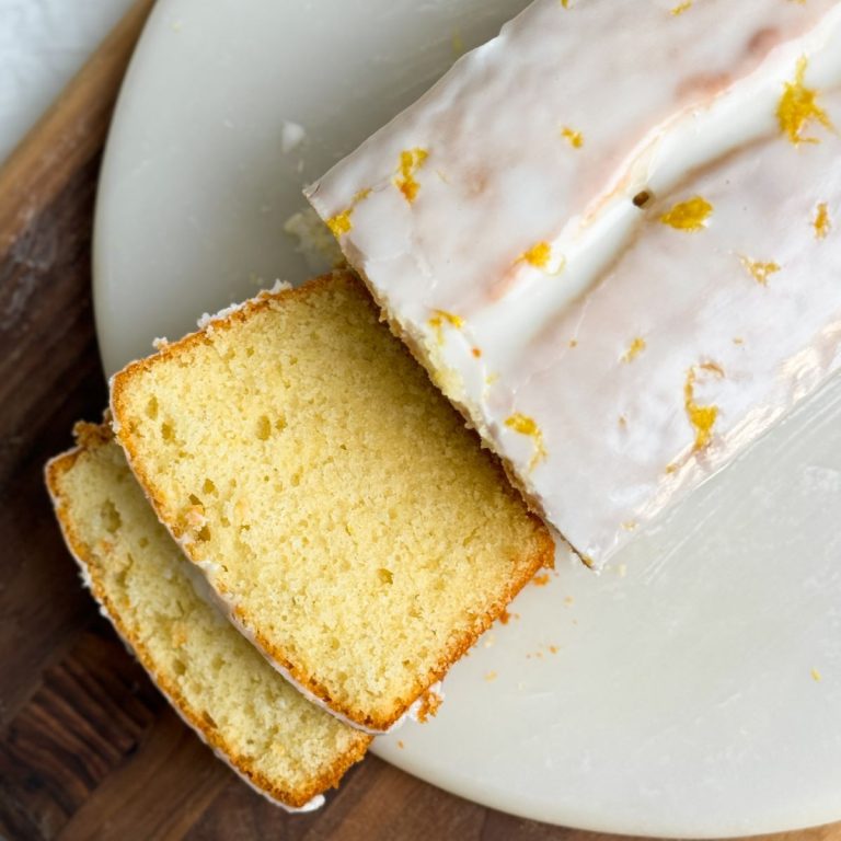 lemon loaf cake on a round marble serving board. cake has a beautiful color and is covered with lemon icing. 2 slices have been cut and are falling down showing the soft and moist interior. close up picture from the top