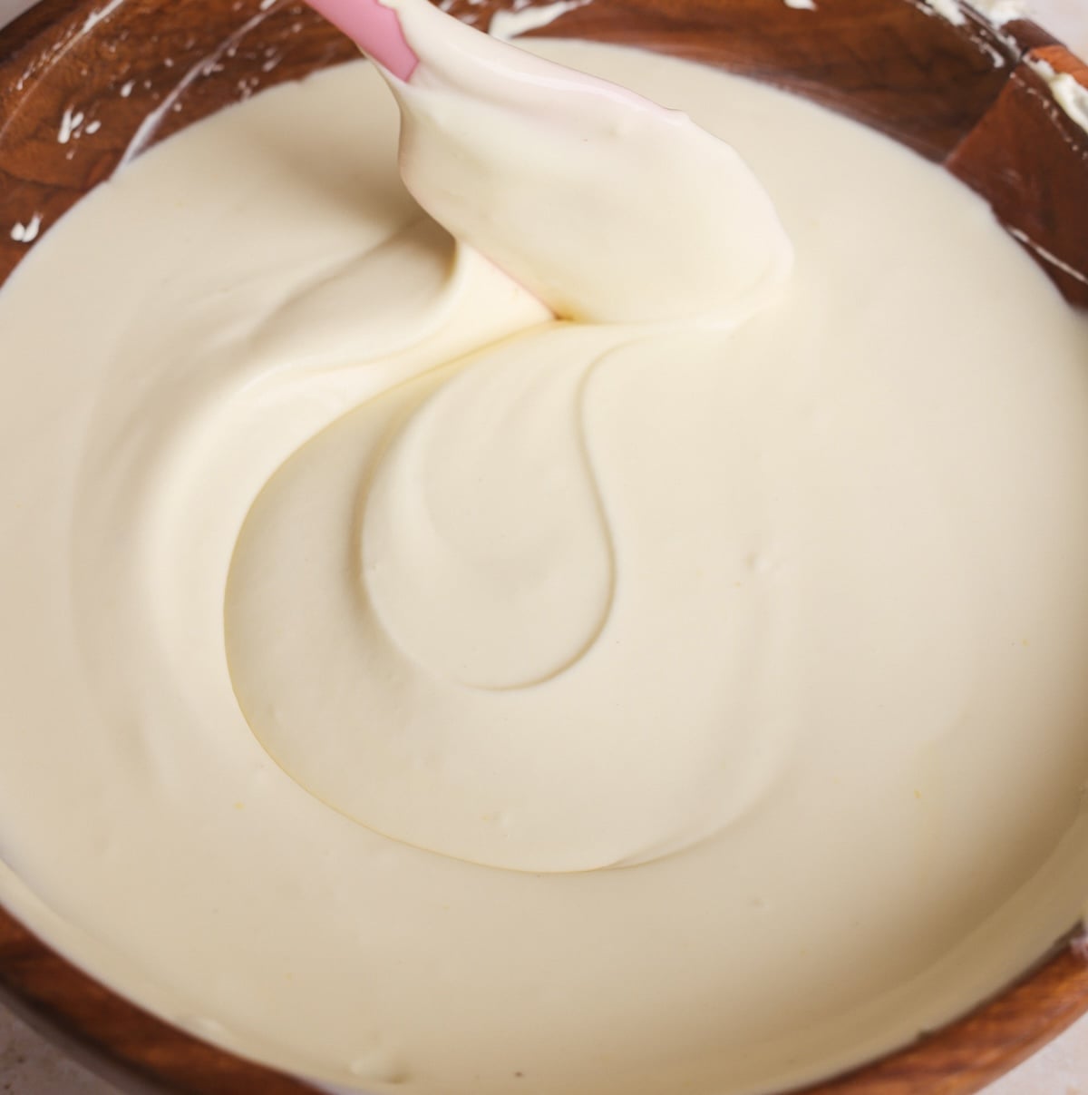 A close-up of creamy mascarpone cream for tiramisu being stirred with a pink spatula in a brown mixing bowl.