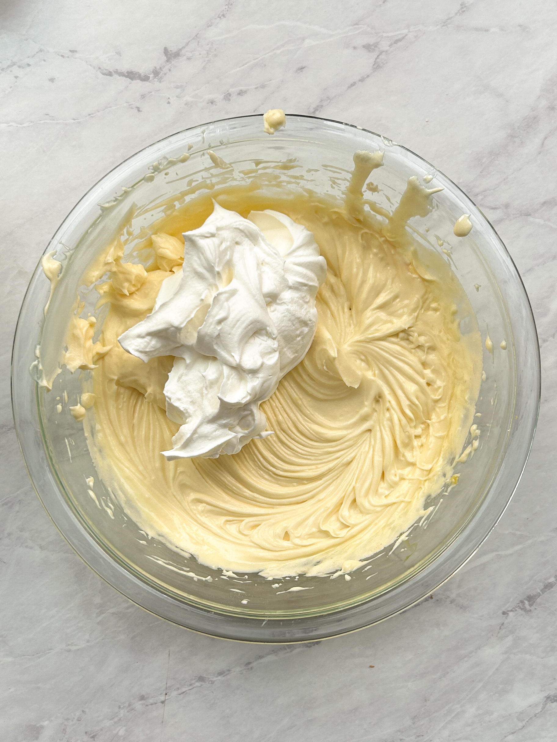 whipped cream added on top of mascarpone and eggs in a bowl