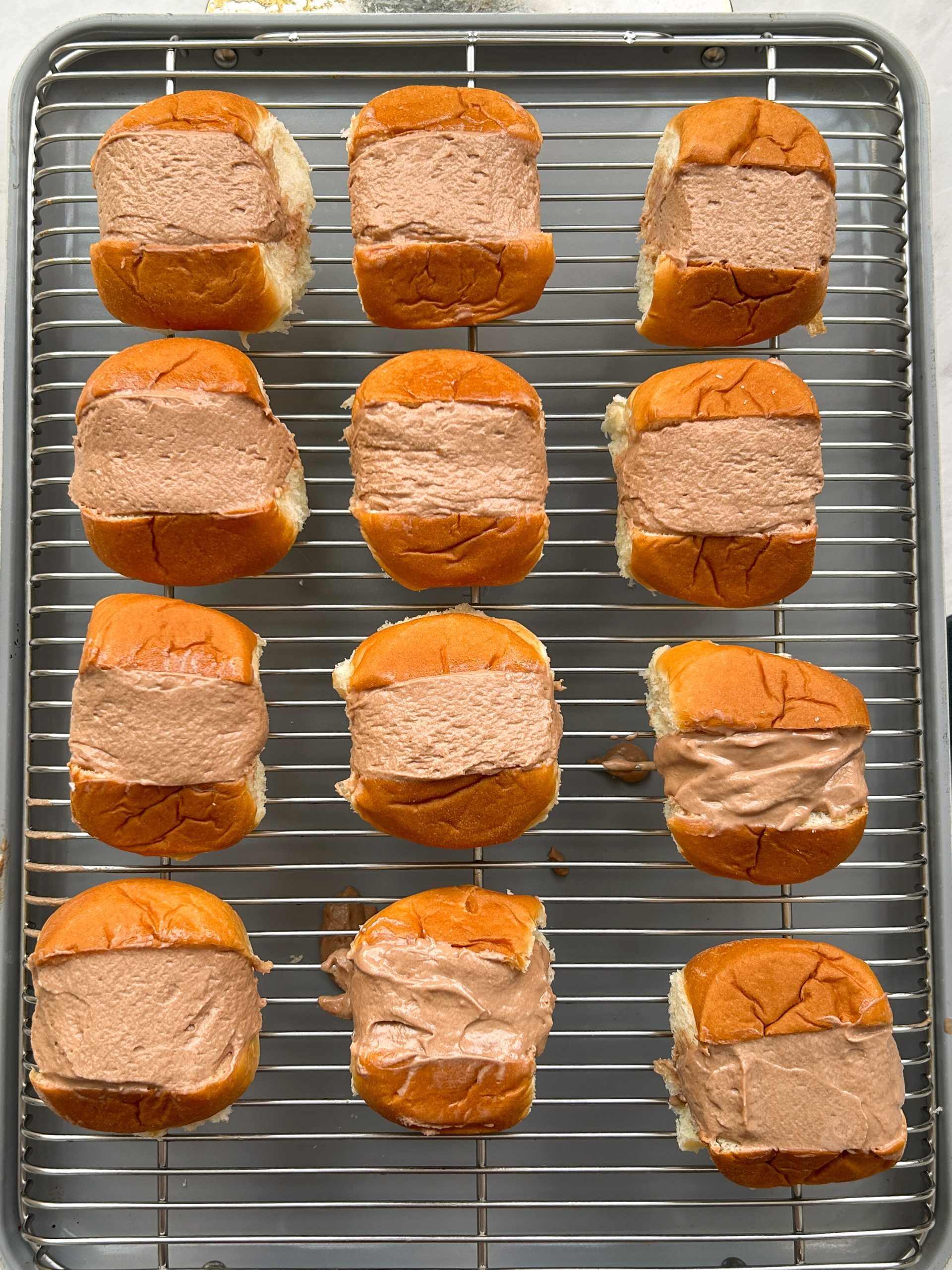 12 buns with a smooth chocolate cream filling in the middle on a wire rack