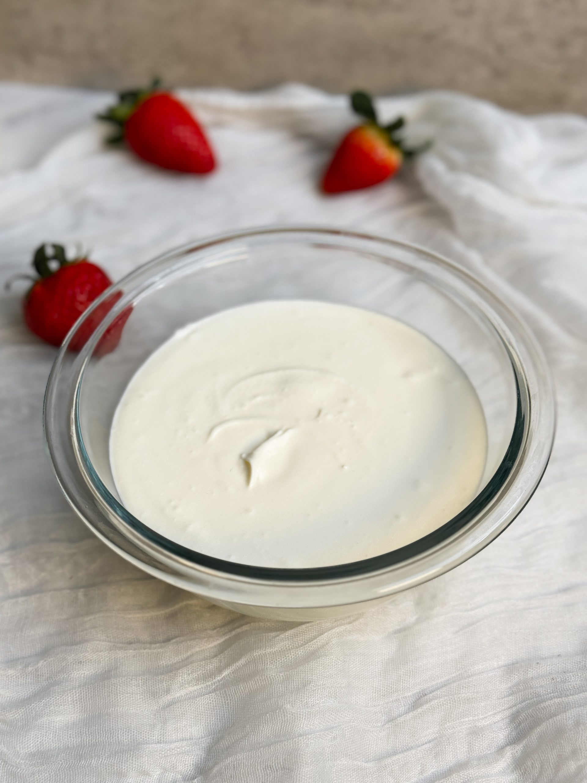 a glass bowl with sour cream. sour cream is thick and creamy. strawberries in background