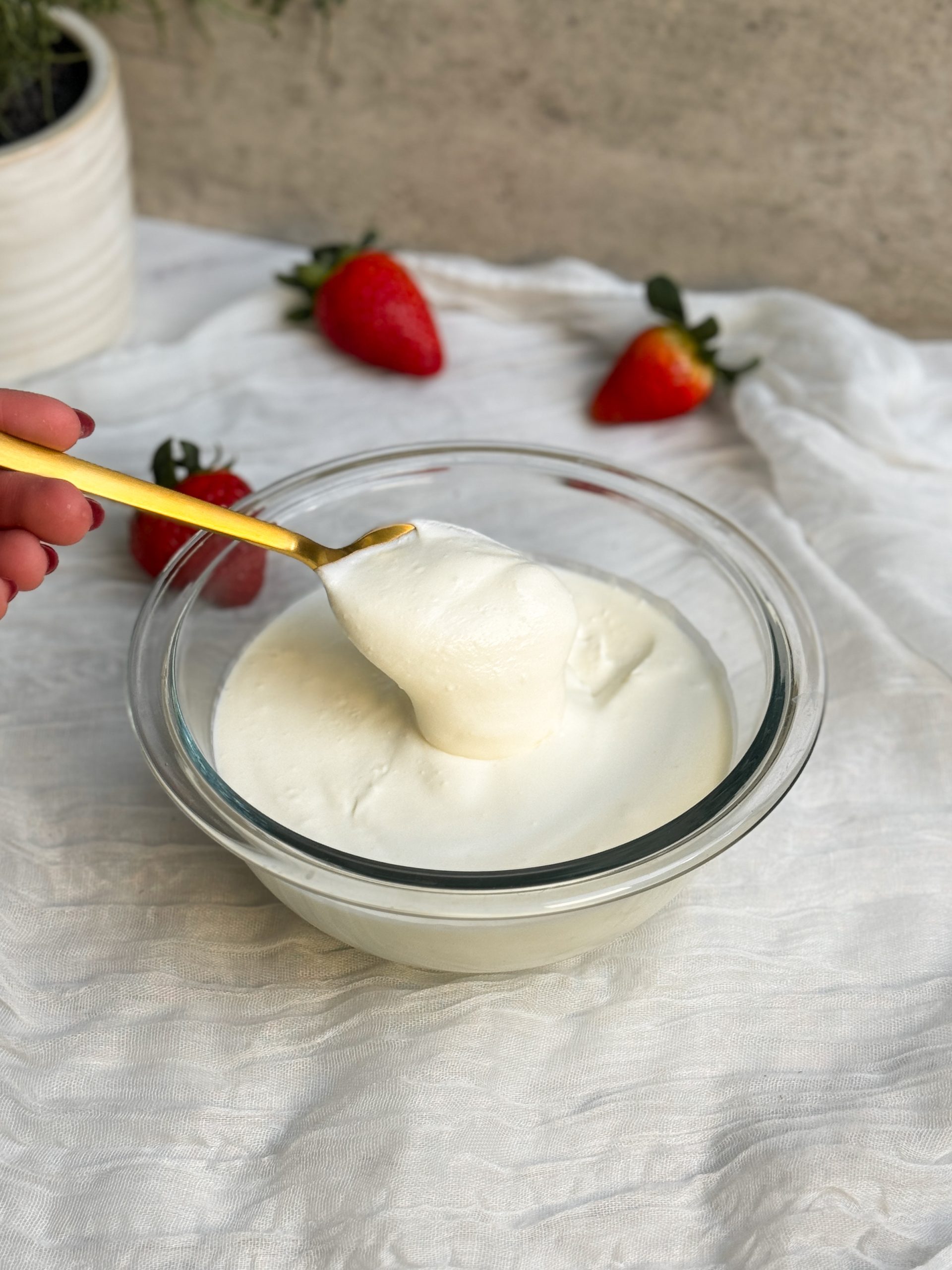 a glass bowl with homemade sour cream. sour cream is thick and creamy. a gold spoon is scooping up some sour cream to show how thick it is