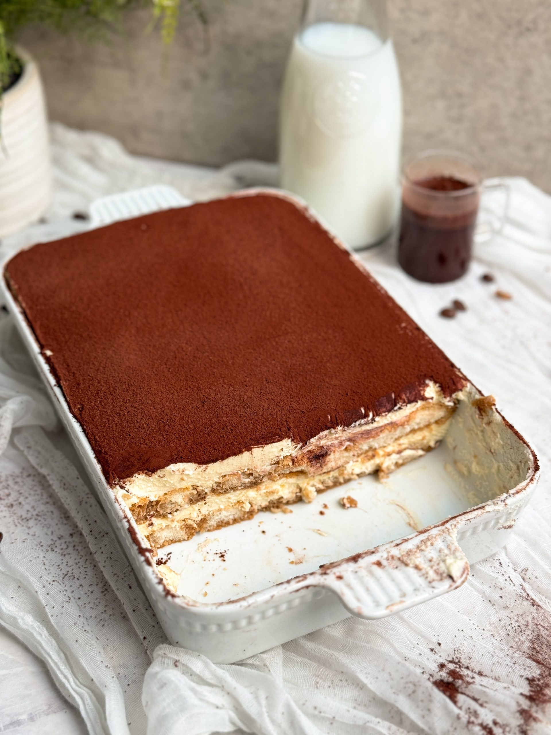 tiramisu in a rectangular dish with a slice taken out to show layers inside