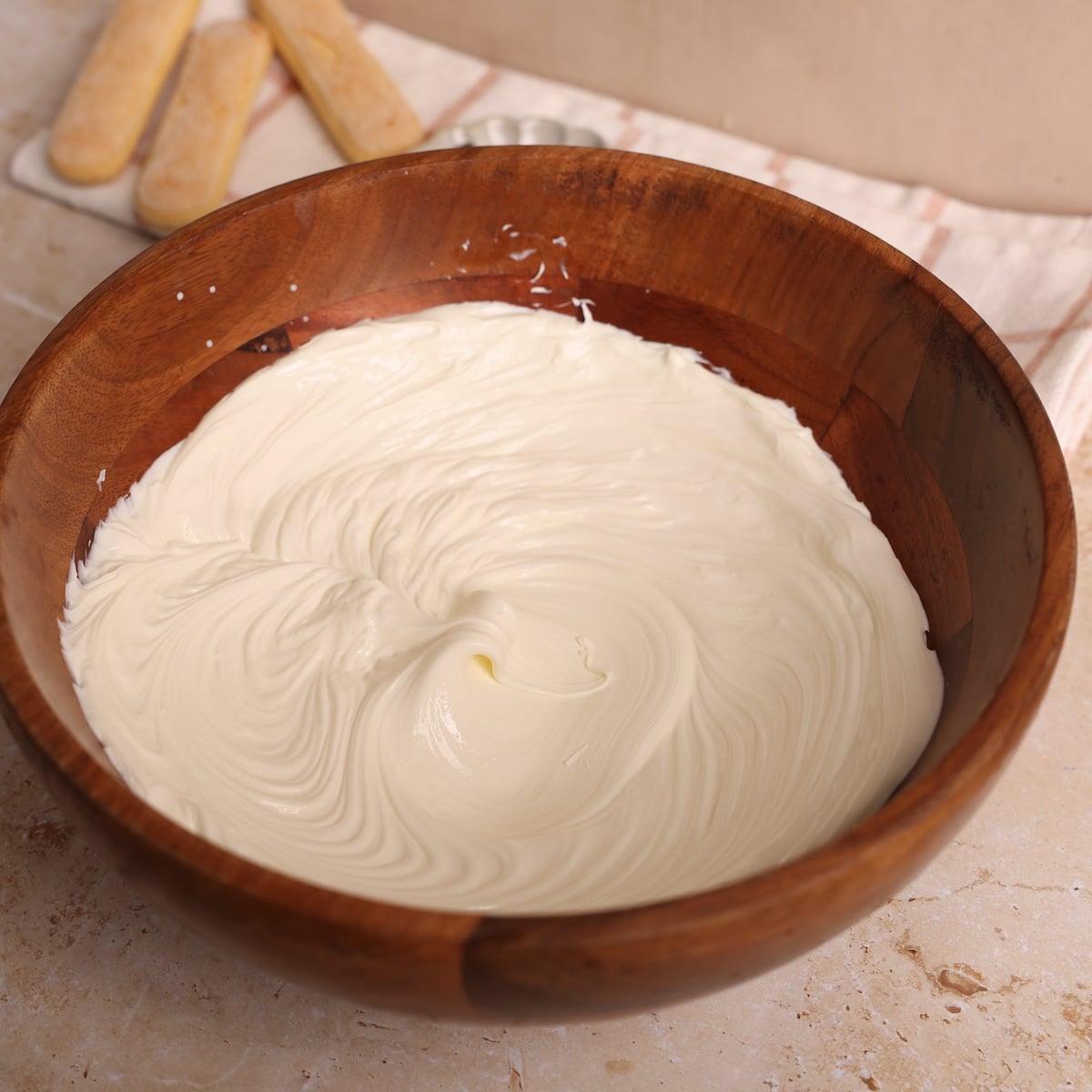 A wooden bowl filled with smooth, creamy whipped mascarpone cheese rests on a countertop