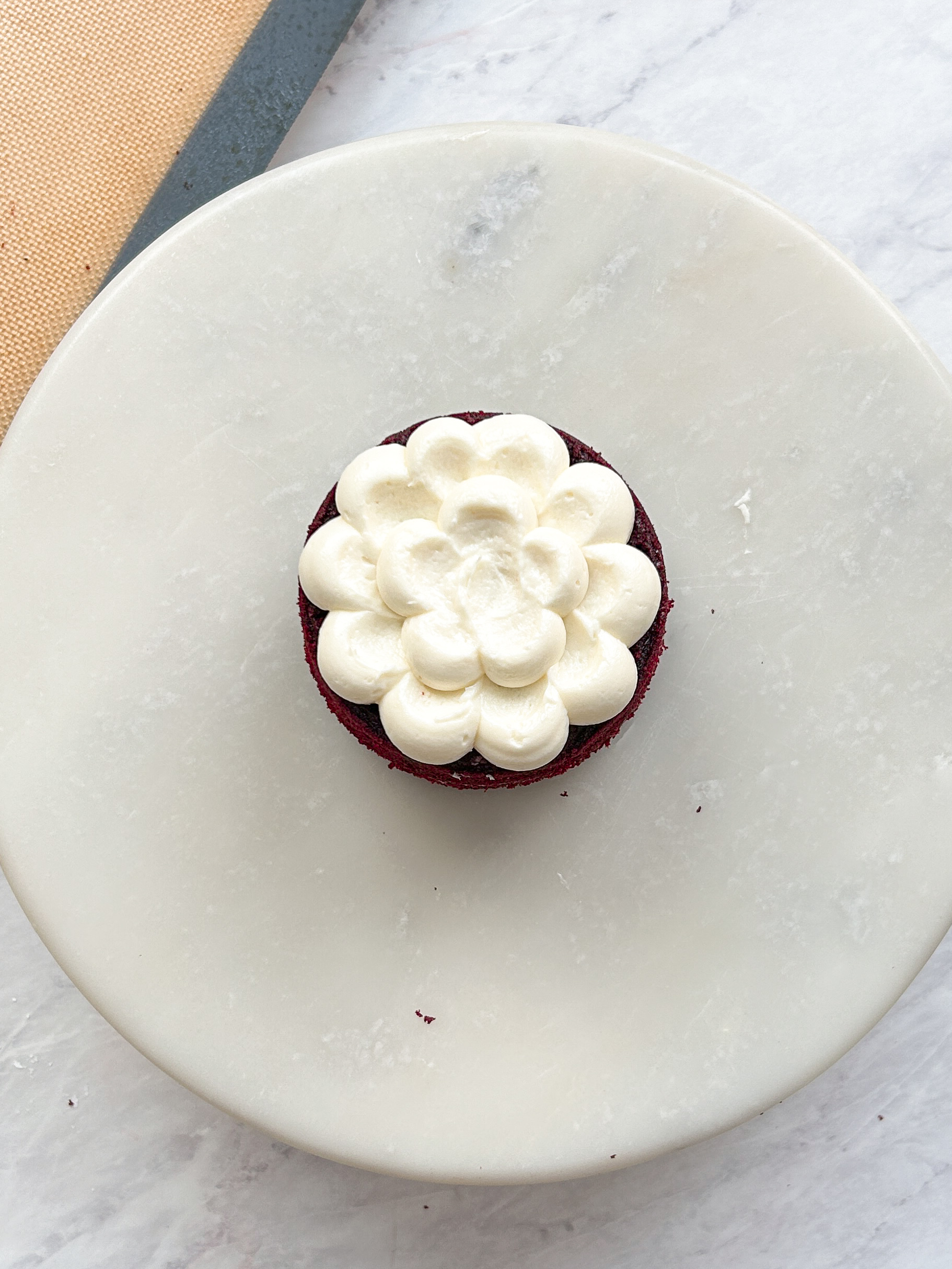 small red velvet cake on a marble serving board with cream cheese dolloped on top