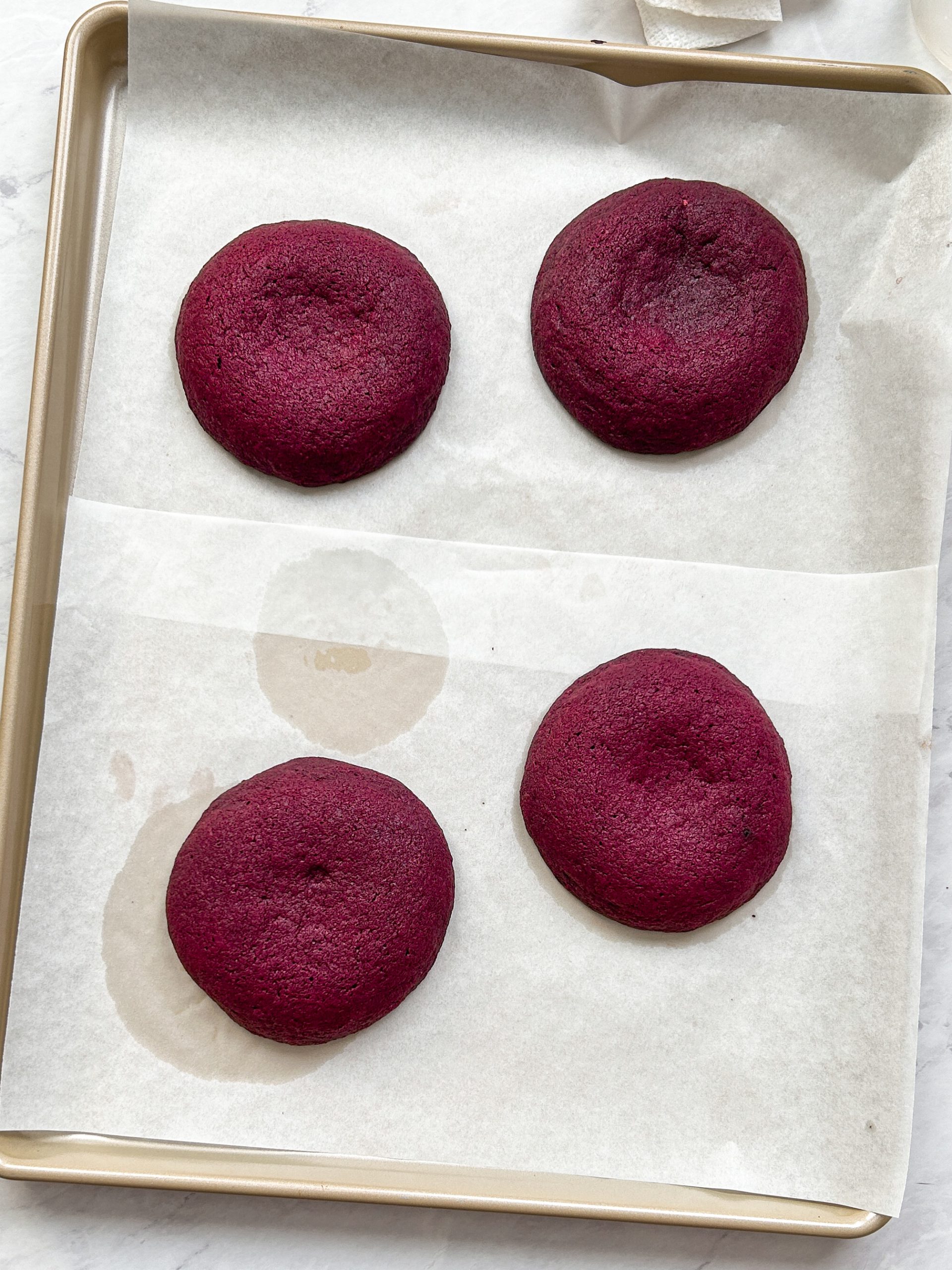 4 large red velvet cookies on a cookie sheet
