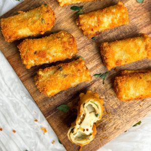 crispy fried lasagna rolls on a wooden cutting board, with one roll cut into half to reveal cheesy center
