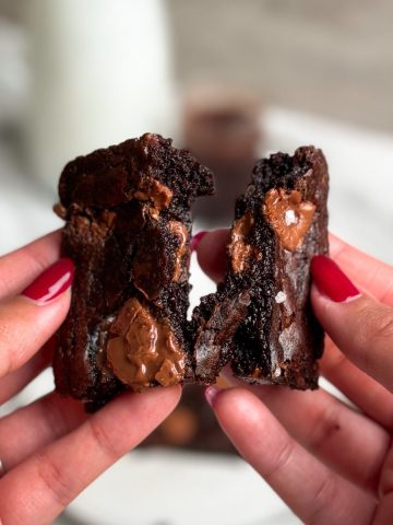 hand holding a single serve brownie and pulling it into 2 halves showing the gooey and fudgy texture inside