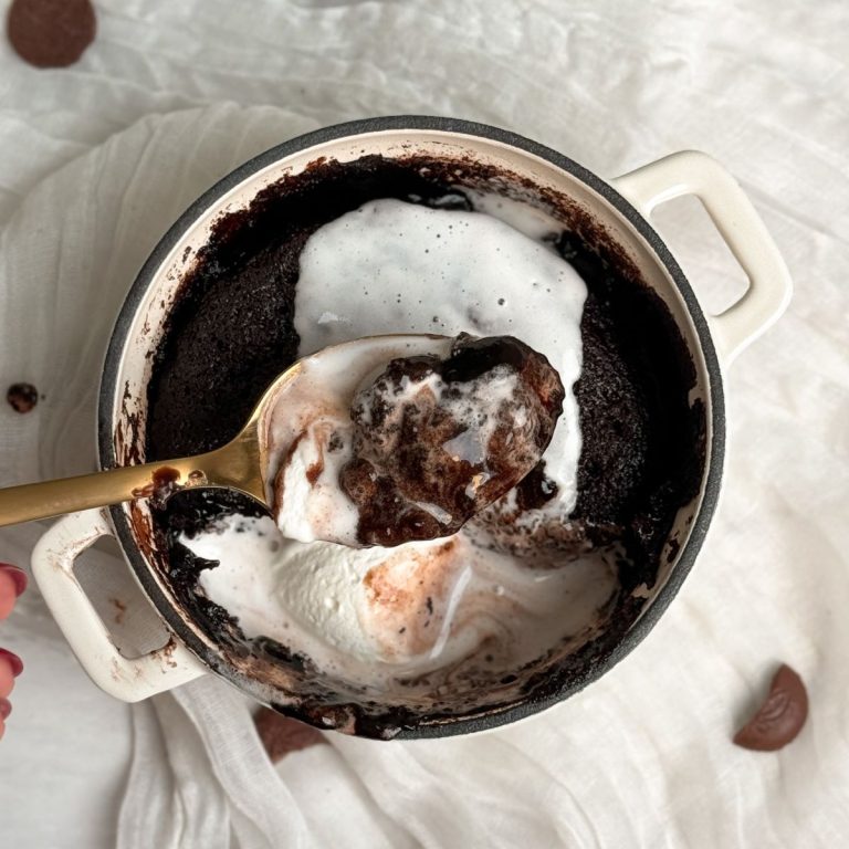 hot fudge chocolate cake with whipped cream on top, with a spoon pulling out a bite showing the molten hot fudge in the cake. hot fudge is melting together with the cream