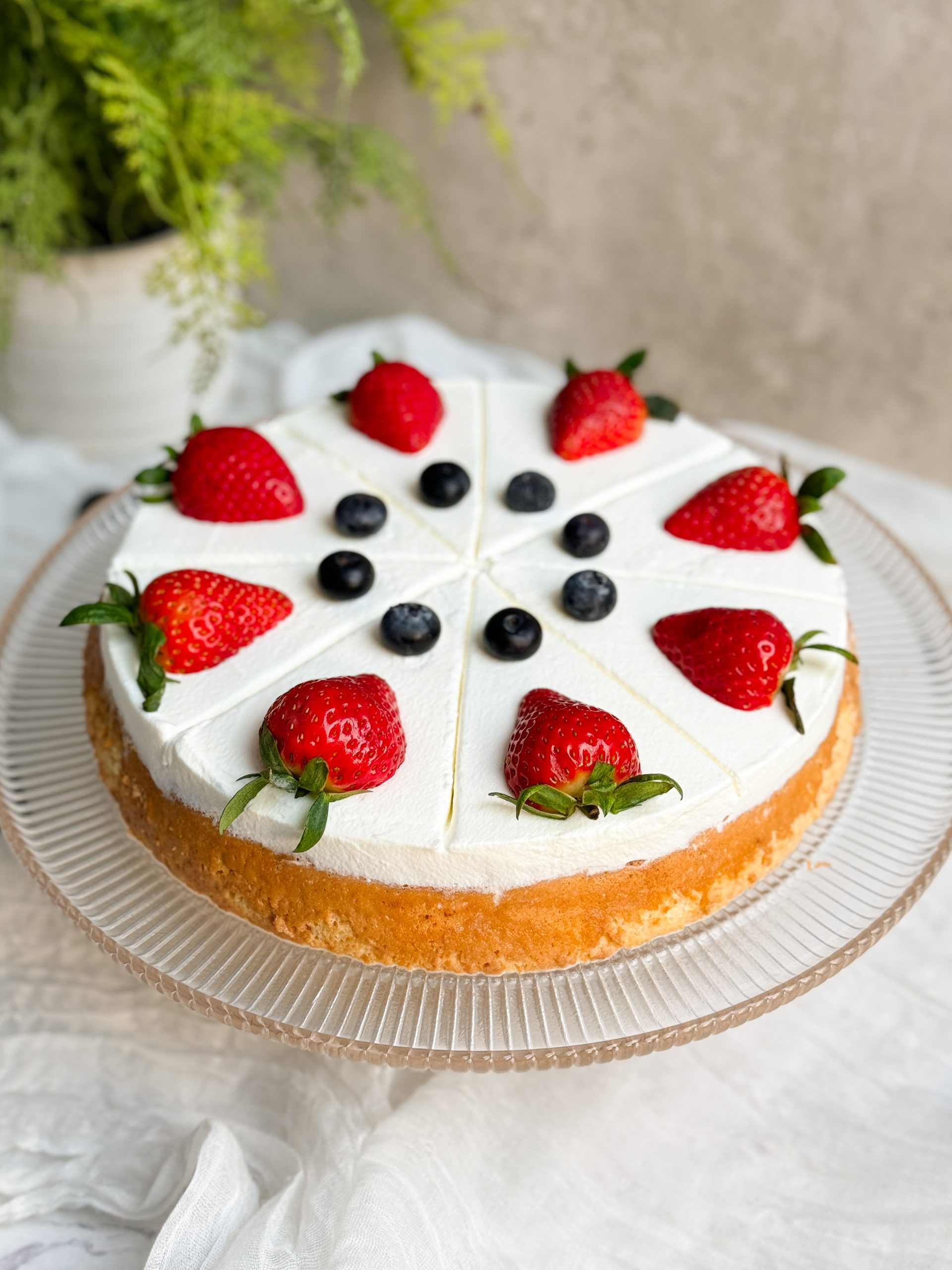 tres leches cake on a glass serving stand. cake is decorated with a thick layer of whipped cream and fresh berries