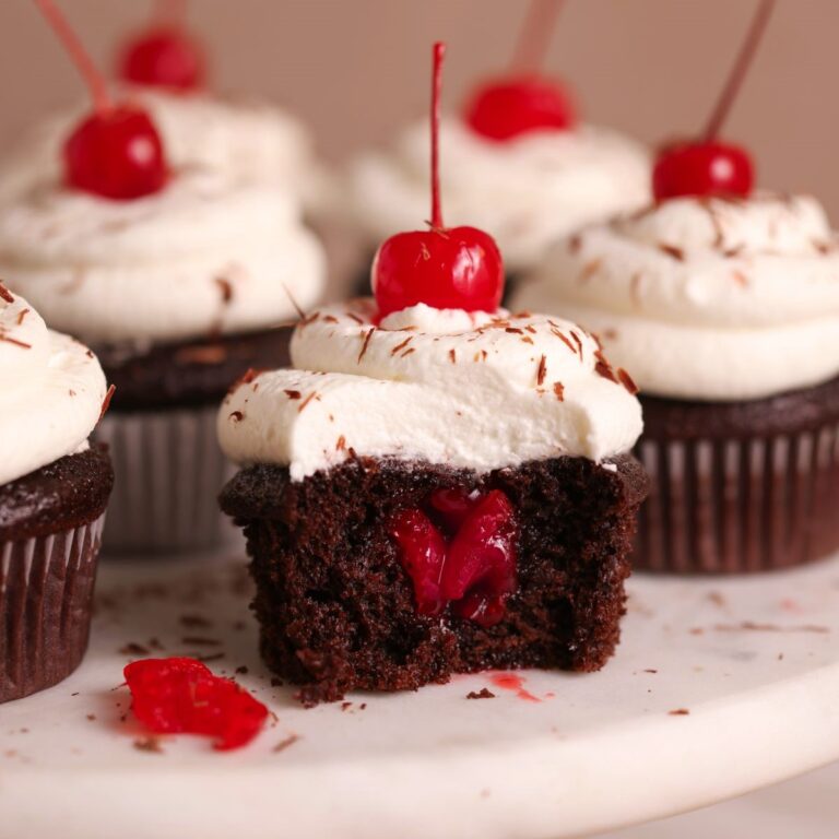 Black forest cupcake on a marble stand with a big bite taken out revealing the cherry filling inside