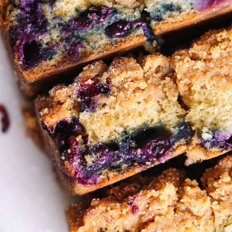 slices of blueberry coffee cake placed sideways next to each other to reveal the layers of buttery crumble and soft cake with lots of blueberries instead. Close up of one slice
