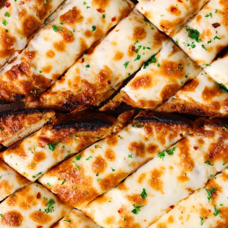 cheesy garlic bread sticks on a wooden cutting board with broiled melted cheese and chopped parsley on top. close up picture from the top